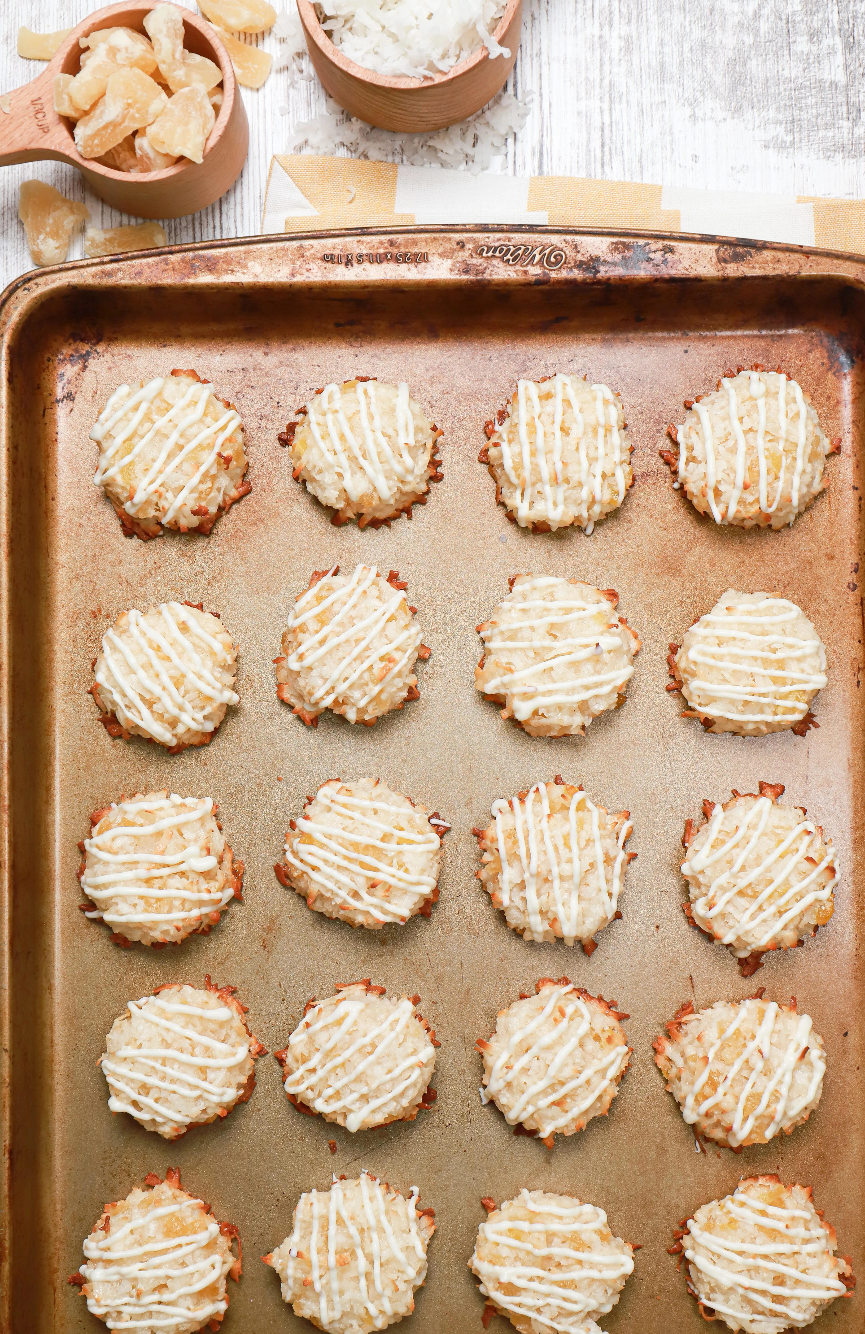Overhead view of white chocolate drizzled pineapple coconut macaroons on a parchment paper lined baking sheet.