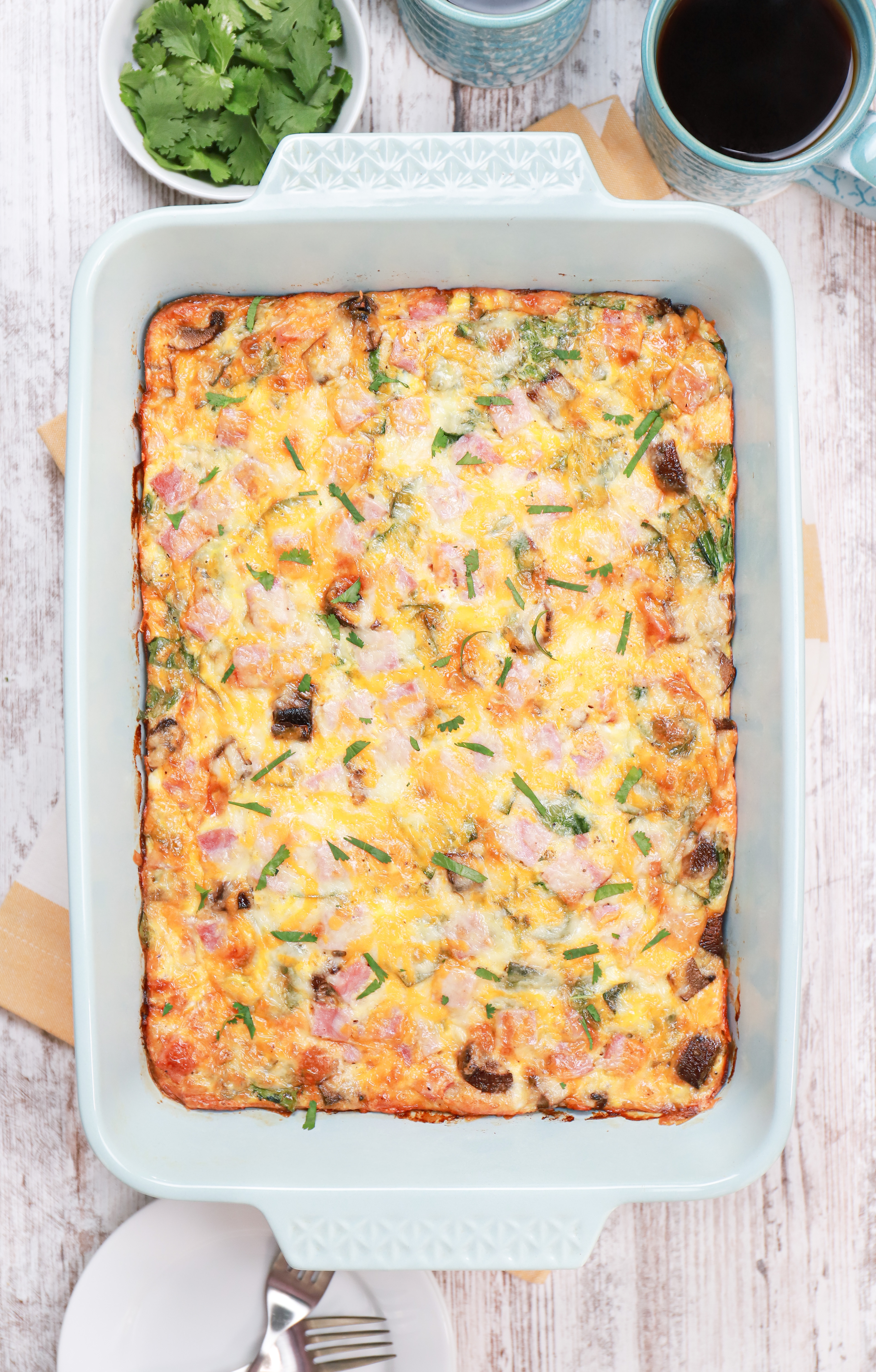 Overhead view of a batch of cheesy ham crescent roll breakfast casserole in a light blue baking dish.