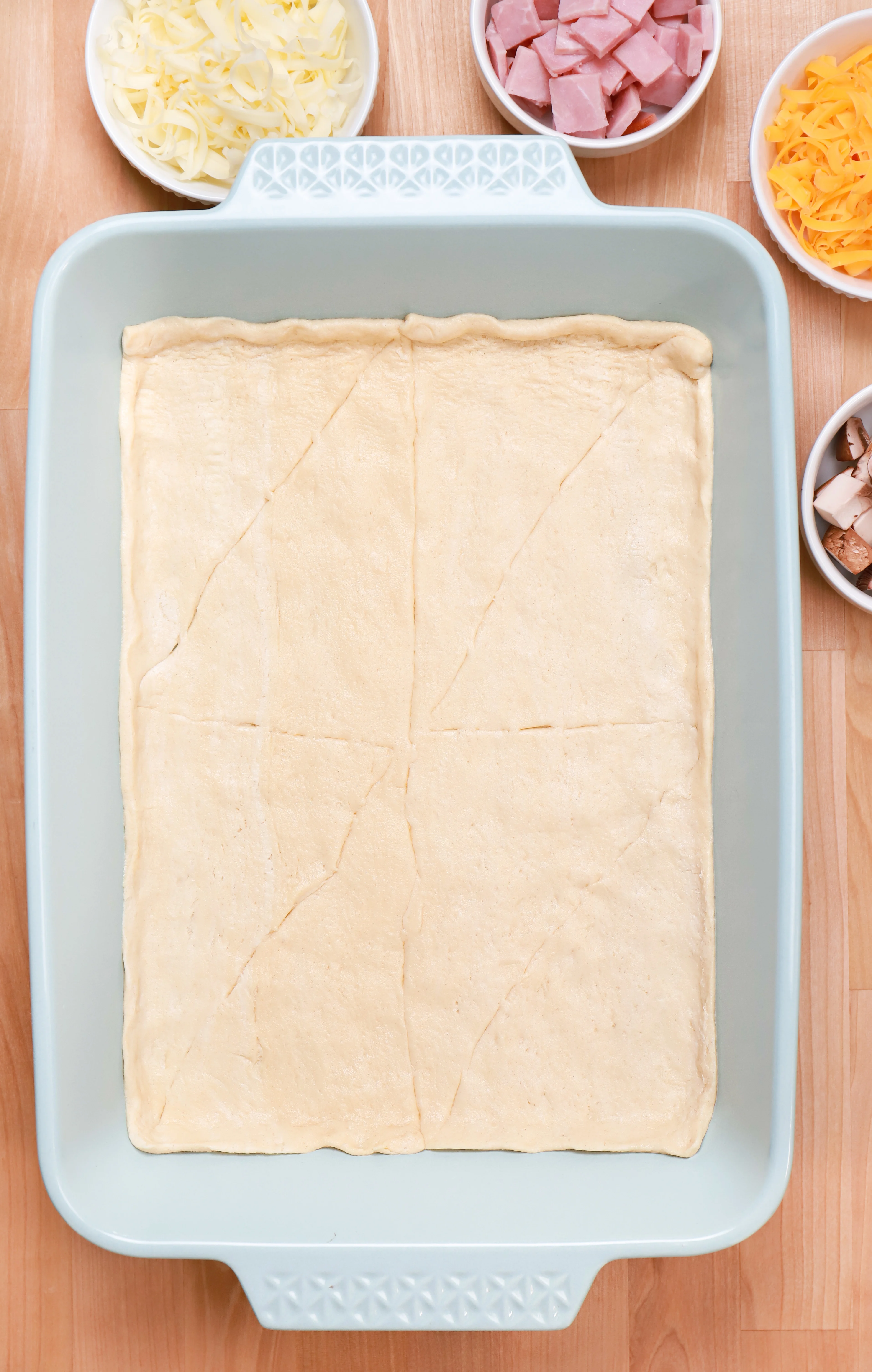 Crescent roll dough pressed into the bottom of a light blue baking dish.