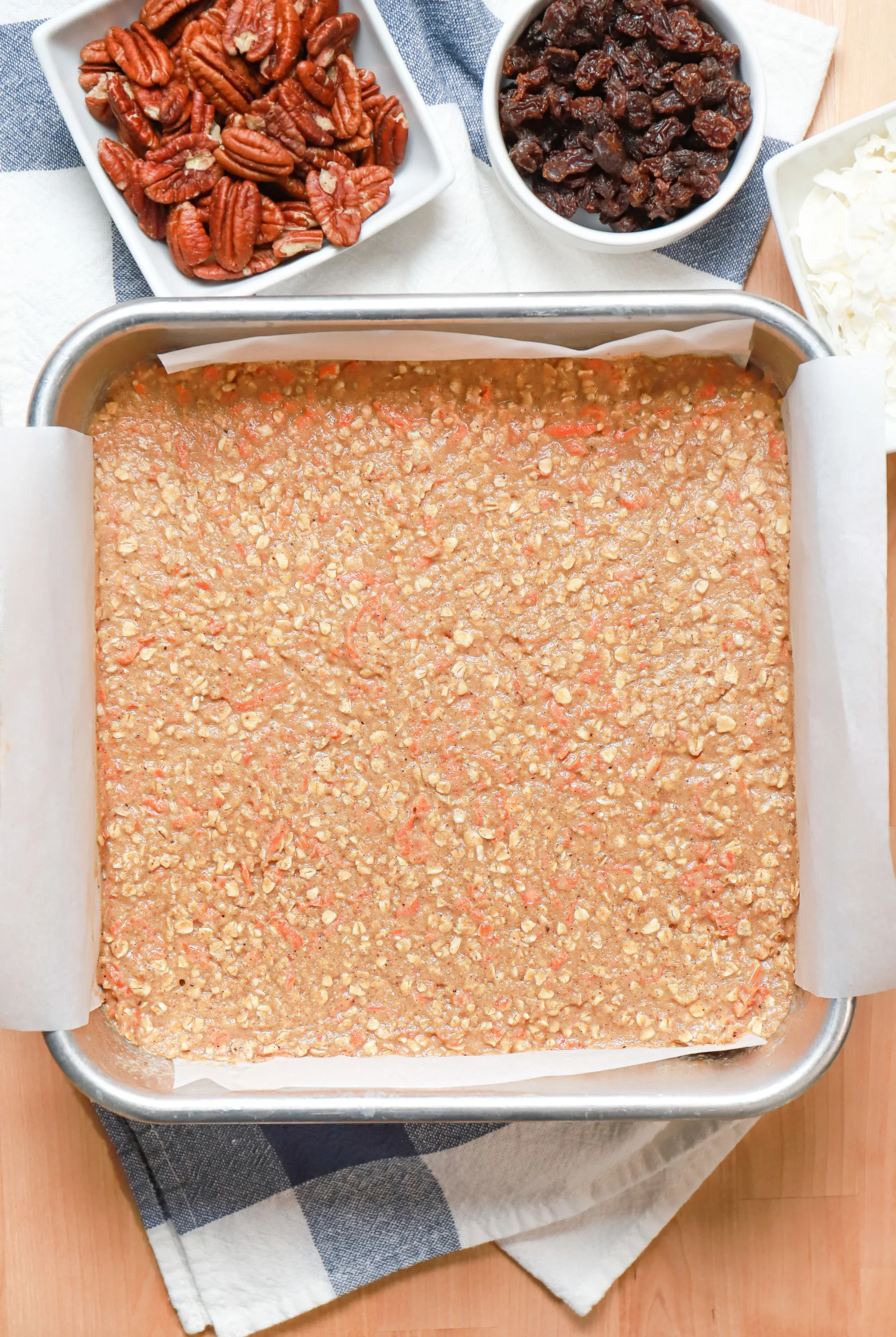 Overhead view of soft baked carrot cake oat bars batter in aluminum baking dish before baking.