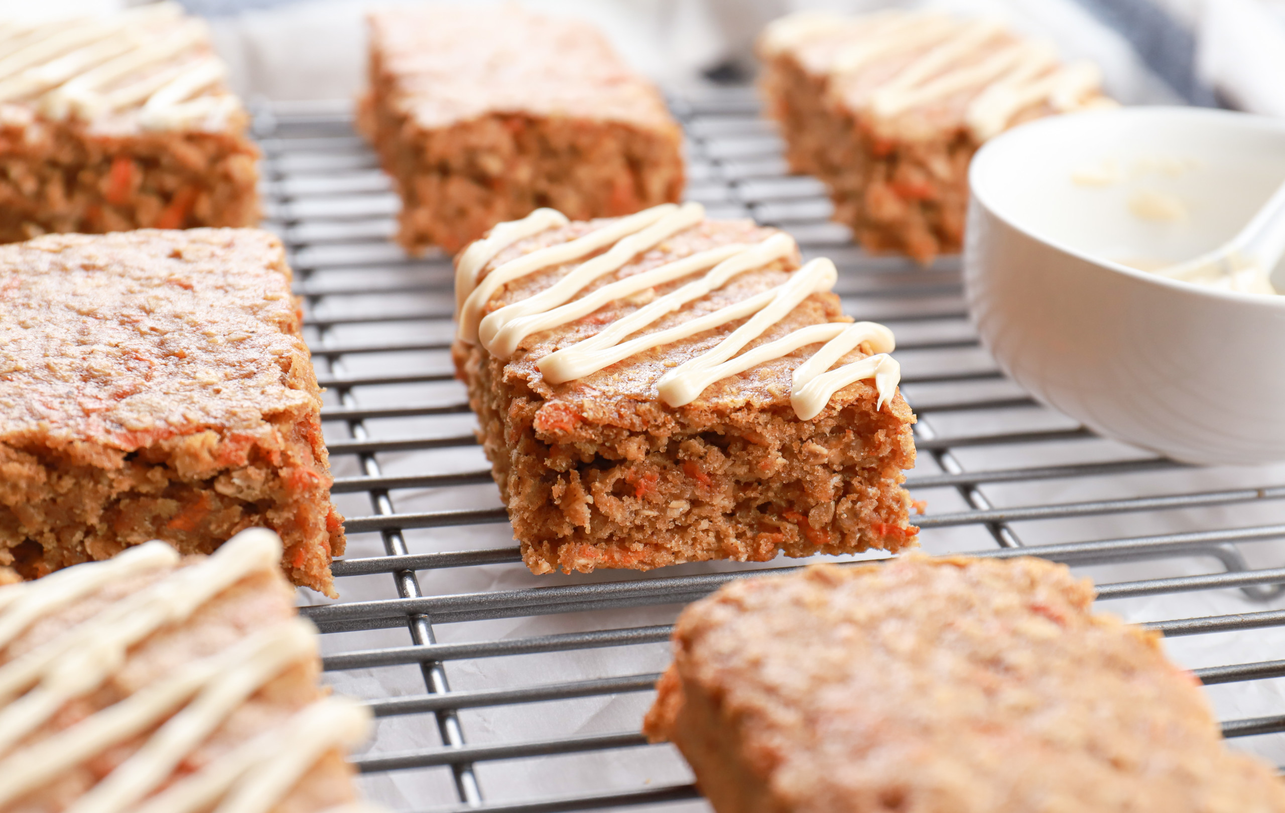 Side view of a soft baked carrot cake oat bar on a cooling rack with more bars in the background.