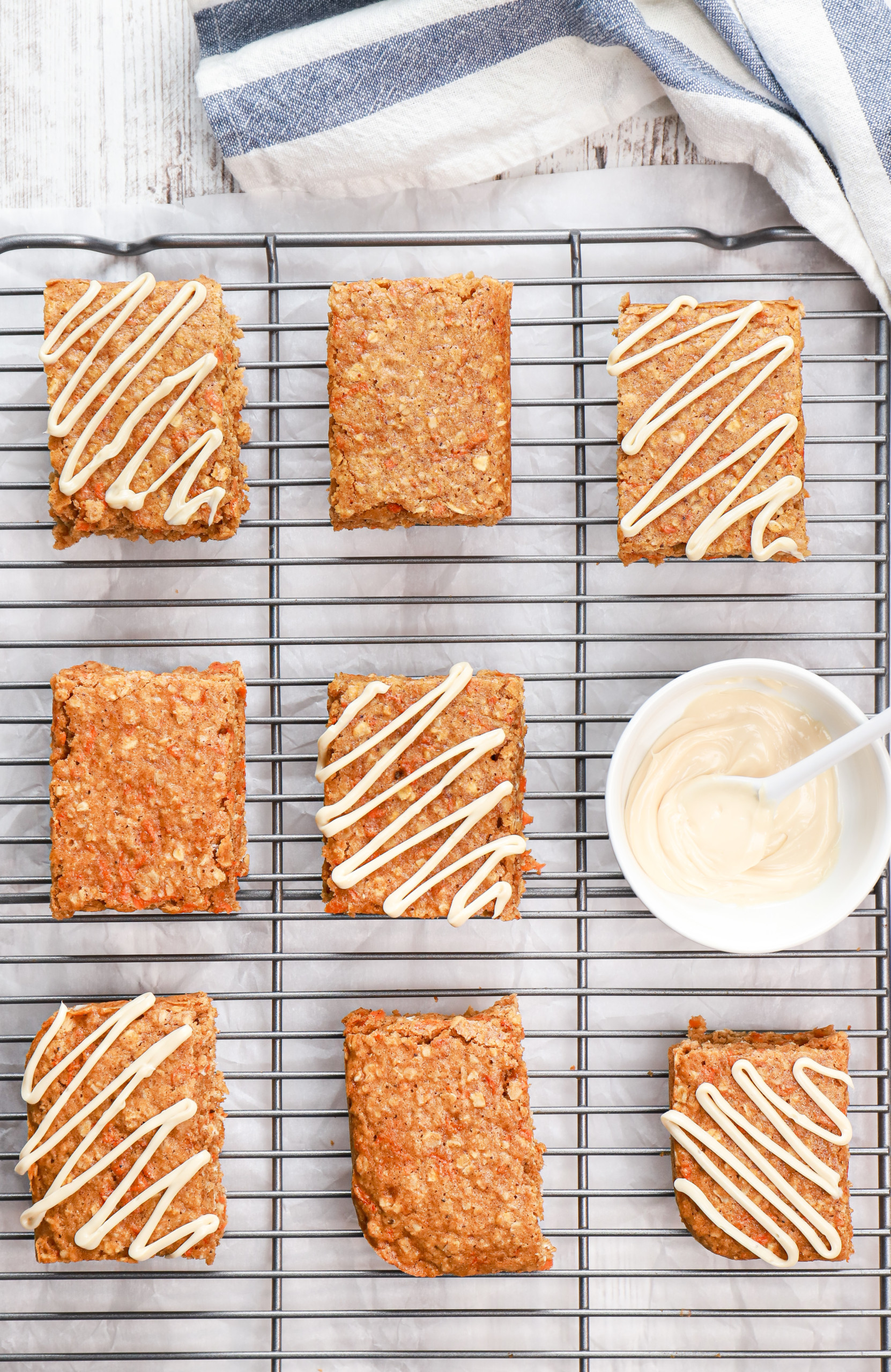 Overhead view of a batch of carrot cake protein oat bars on a cooling rack with some of them drizzled with a cream cheese glaze.