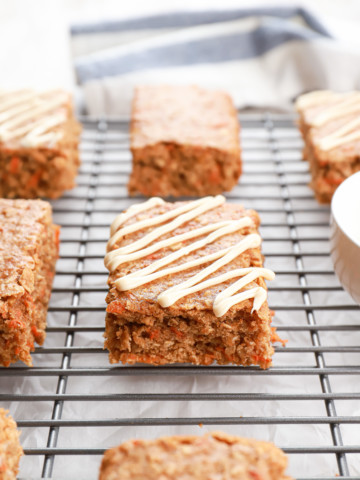 Up close side view of a cream cheese drizzled healthy carrot cake oat bar sitting on a cooling rack.