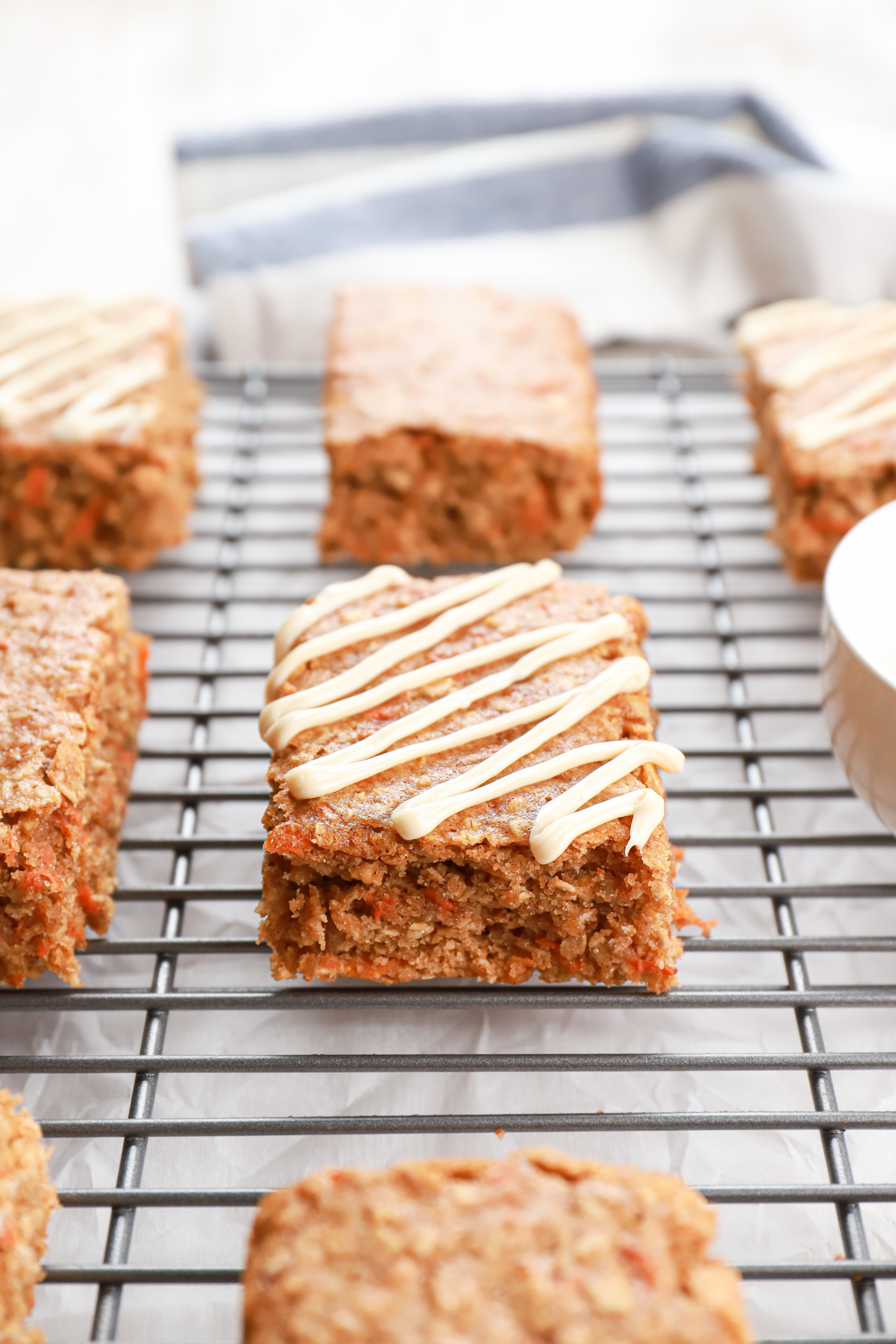 Up close side view of a cream cheese drizzled healthy carrot cake oat bar sitting on a cooling rack.