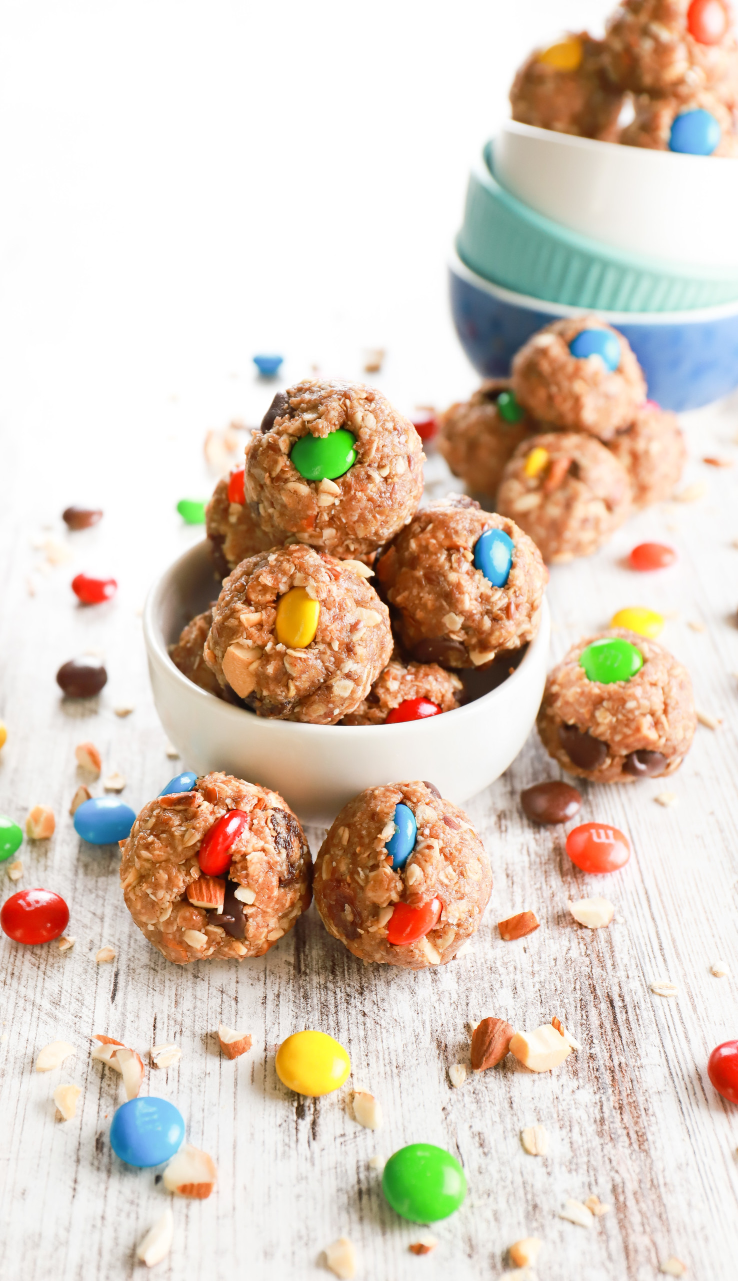 A small white bowl full of almond butter trail mix bites surrounded by additional trail mix bites.