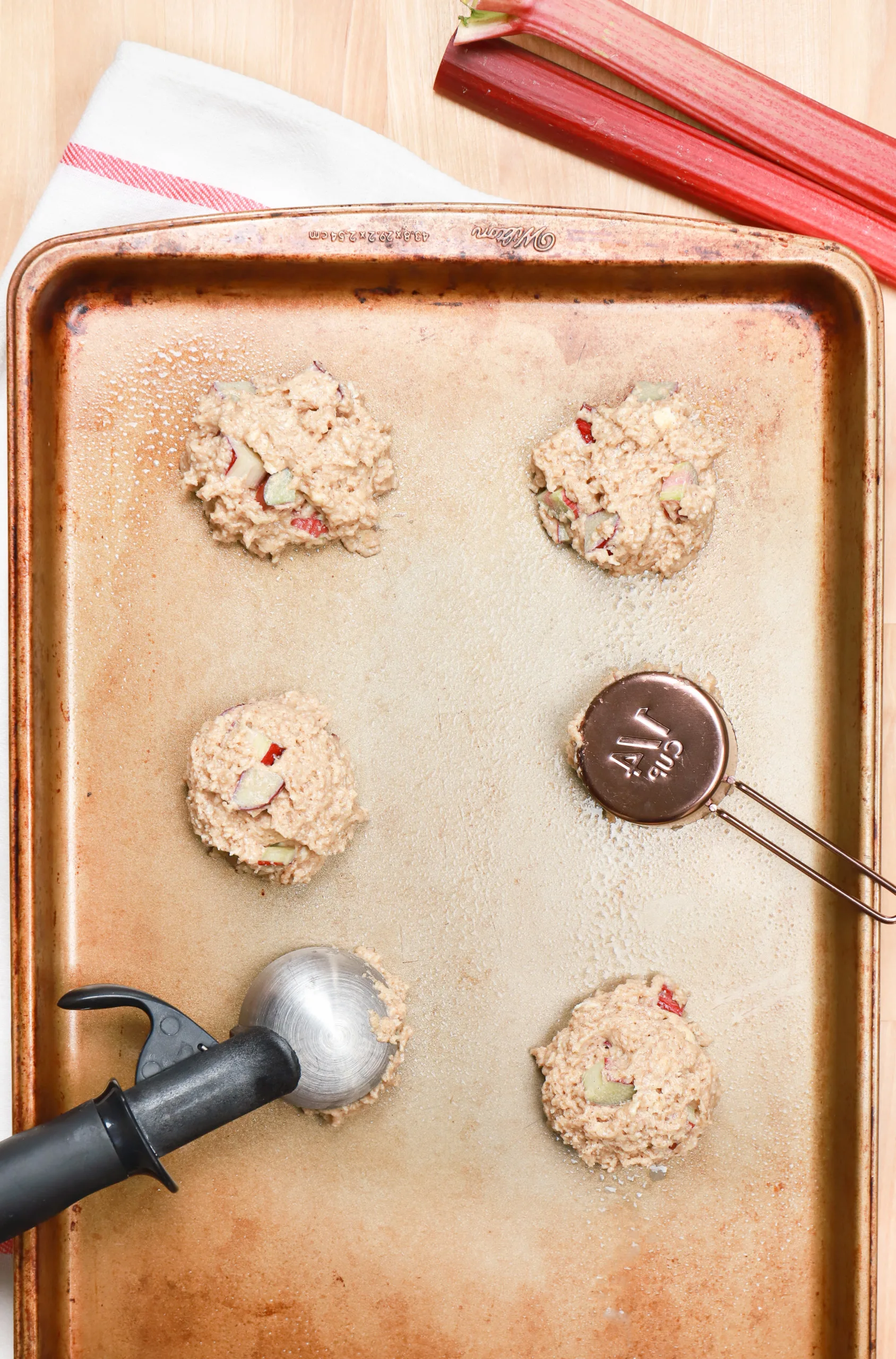 Portioned out rhubarb fritter batter on an aluminum baking sheet.