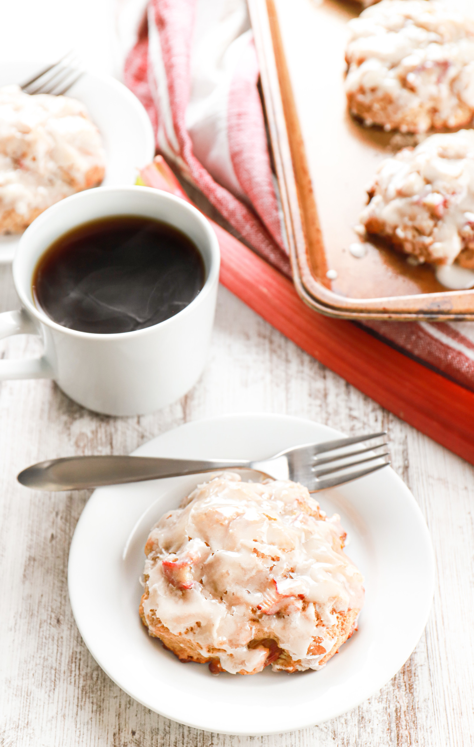 Overhead view of a baked rhubarb fritter on a small white plate with remaining fritters on a baking sheet in the background.