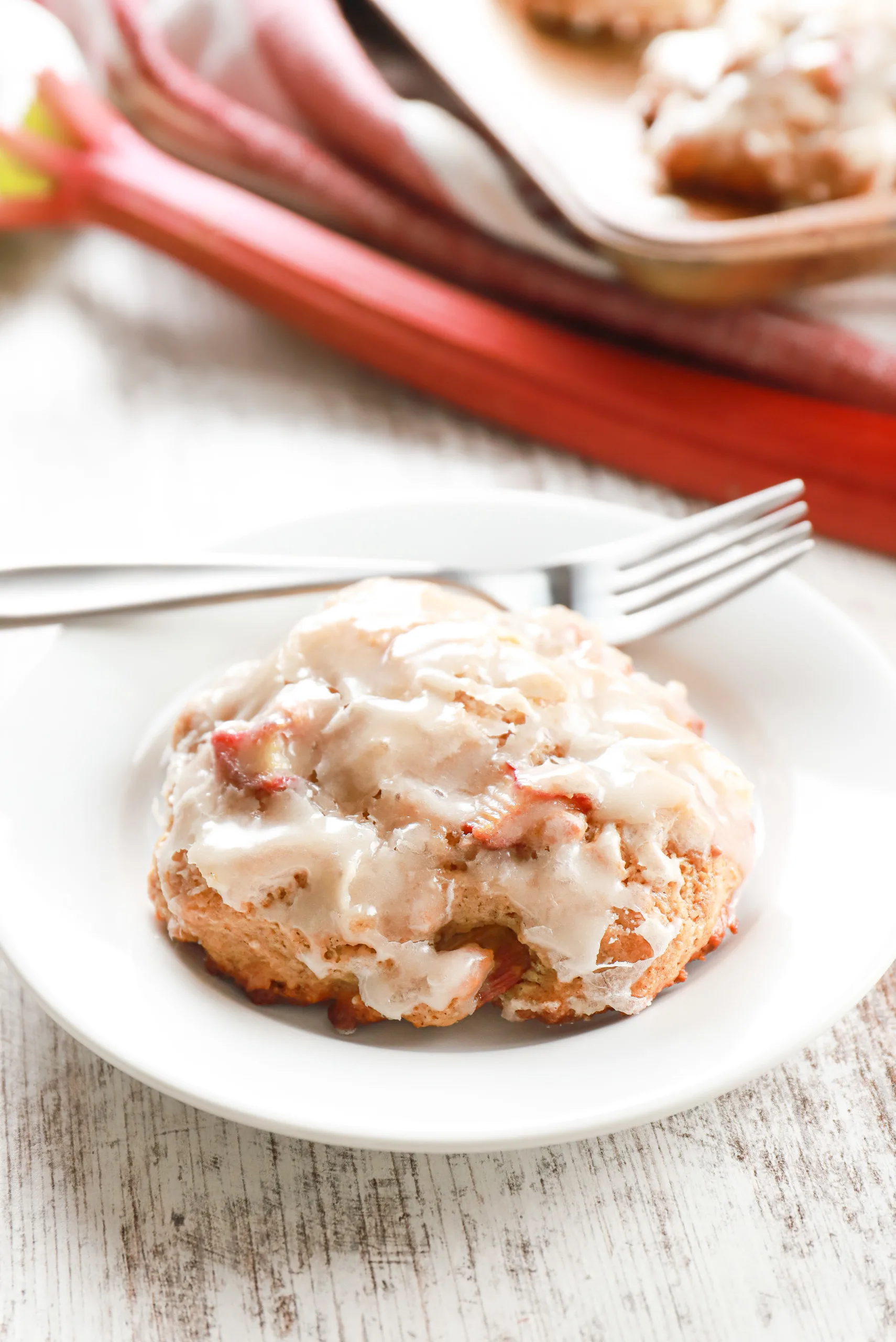 Baked rhubarb fritter on a small white plate with remaining fritters on a baking sheet in the background.