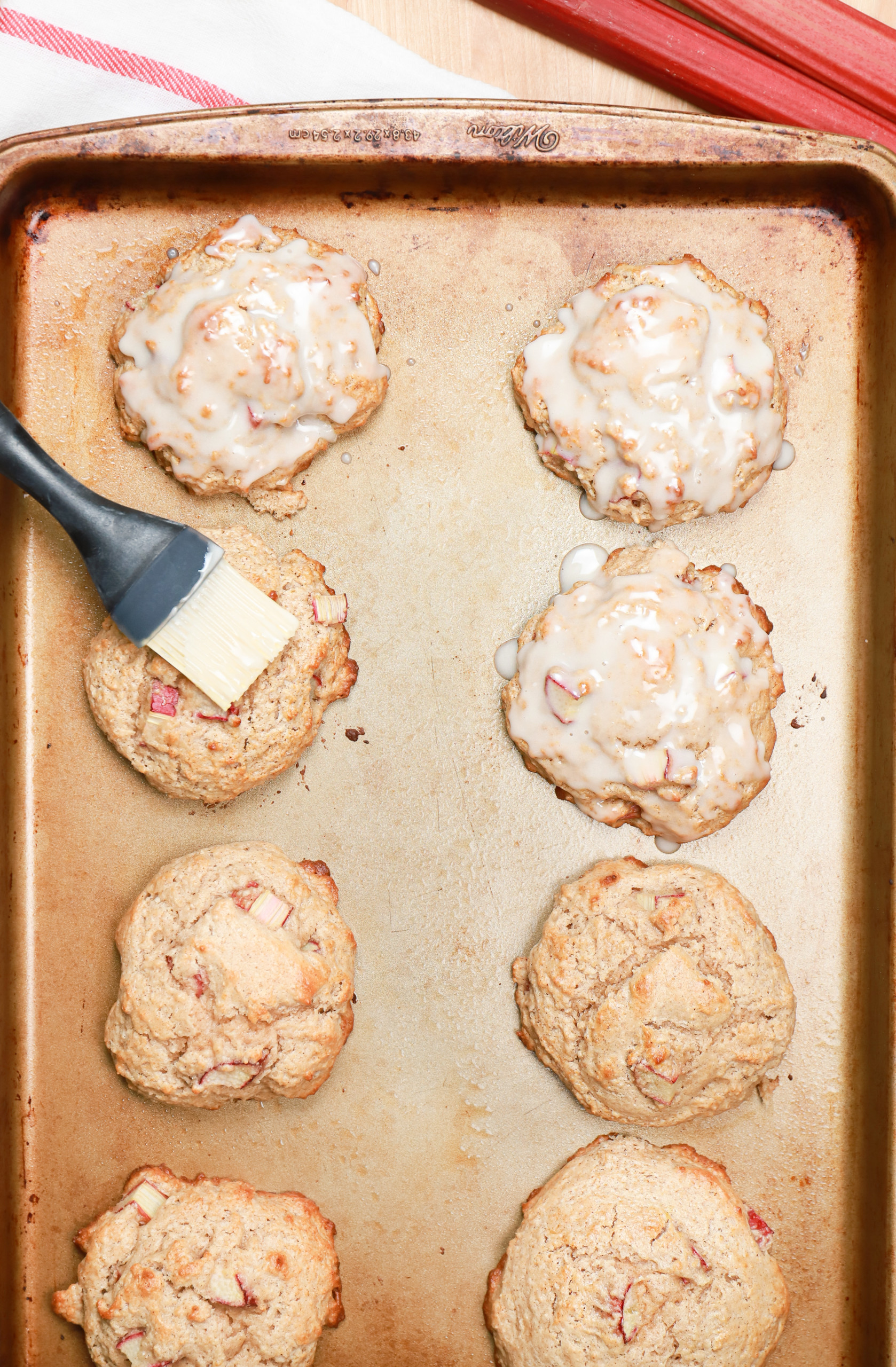 Overhead view of baked rhubarb fritters being brushed with confectioner's sugar glaze.