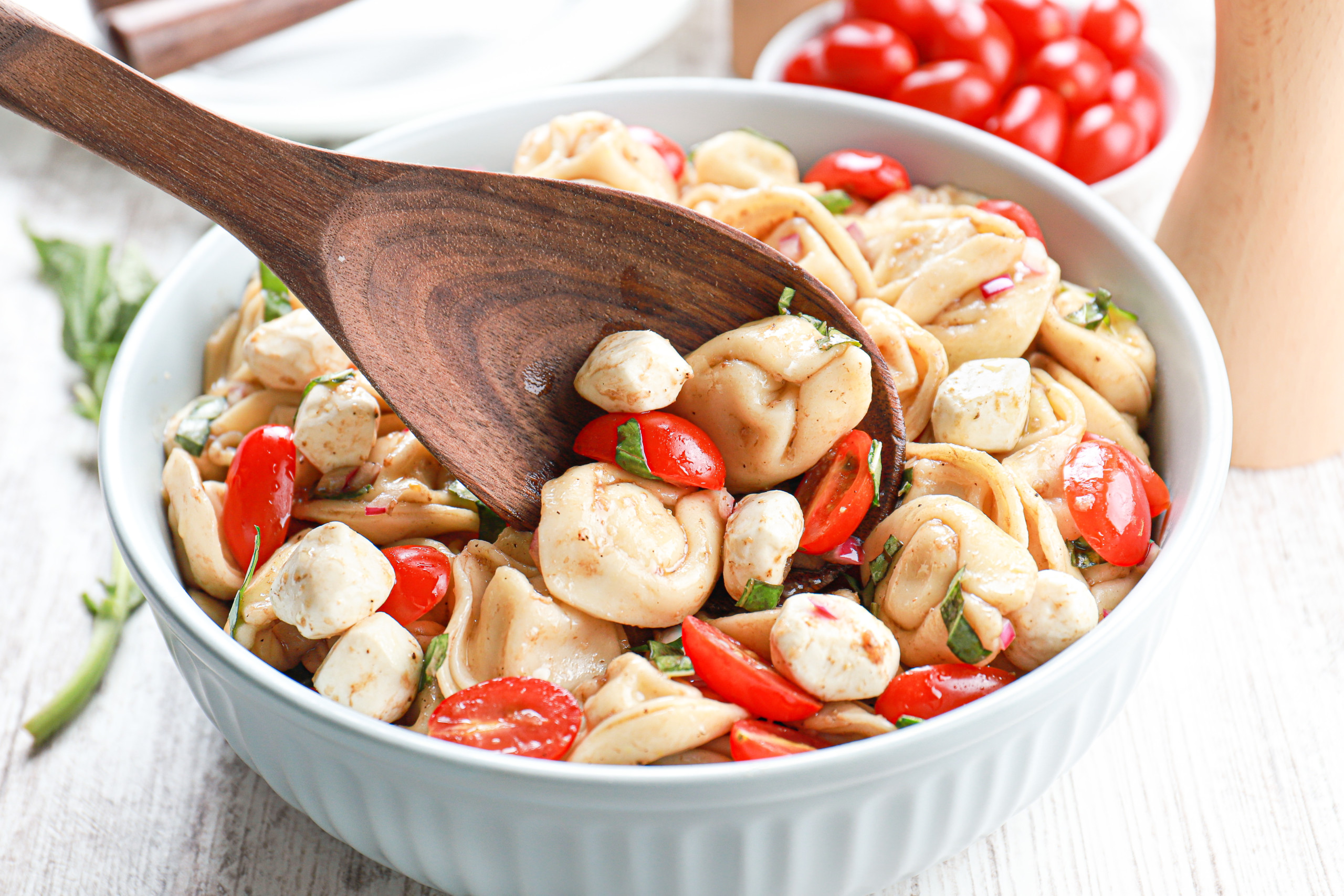 Up close view of a dark wooden spoon full of caprese tortellini salad.
