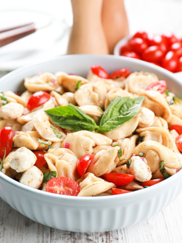 Up close side view of a light blue bowl full of caprese tortellini salad.