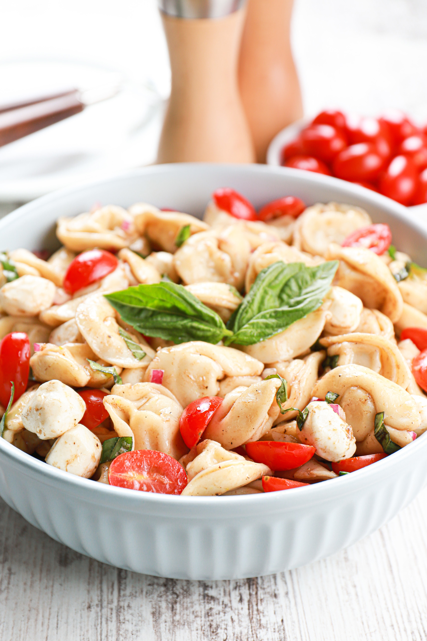 Up close side view of a light blue bowl full of caprese tortellini salad.