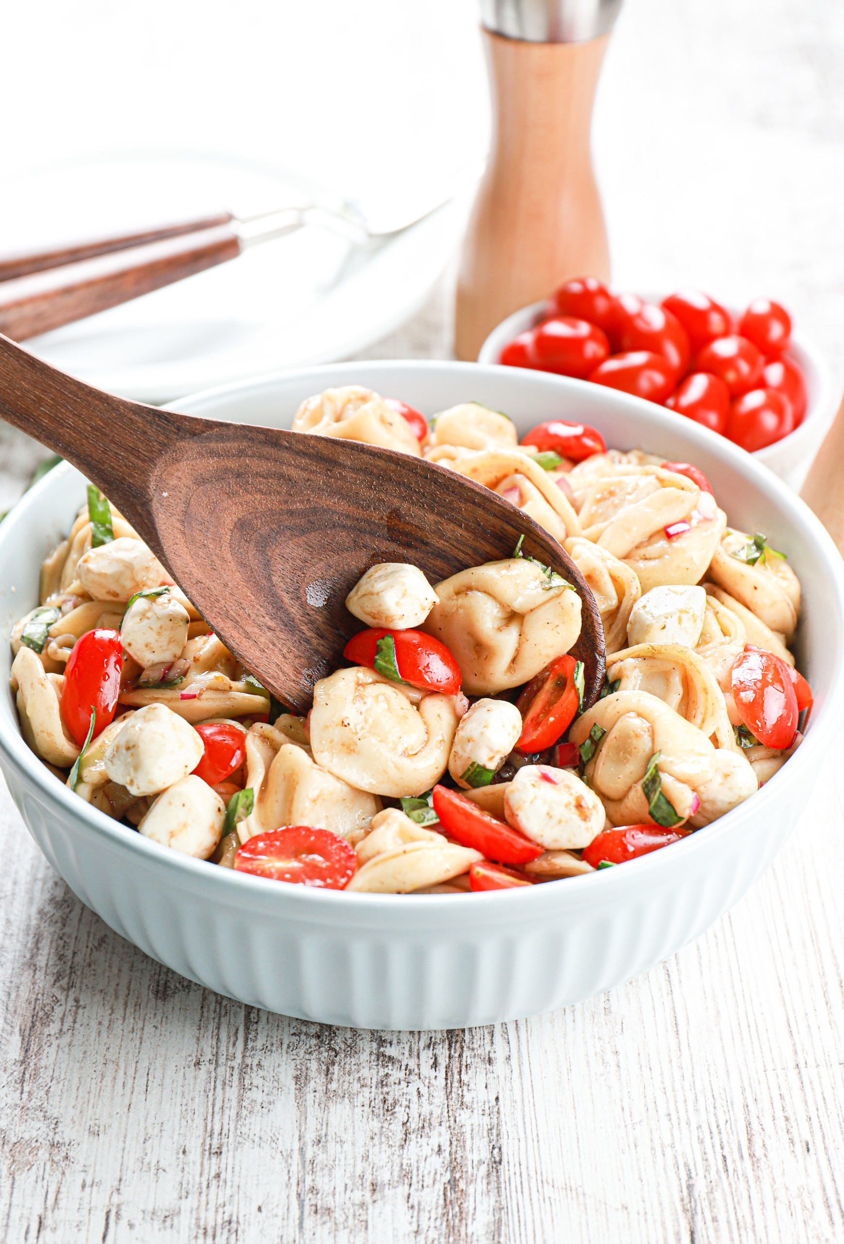 Wooden spoonful of caprese tortellini salad in a light blue bowl.
