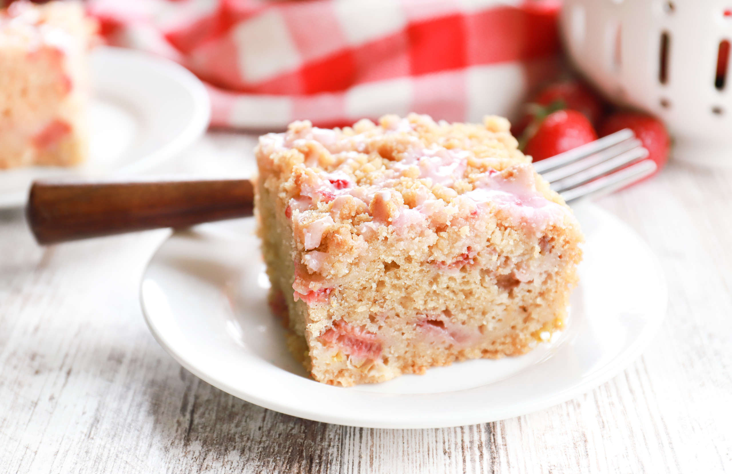 Side view of a piece of strawberry rhubarb crumb cake on a small white plate with a wooden handled fork resting on the plate.