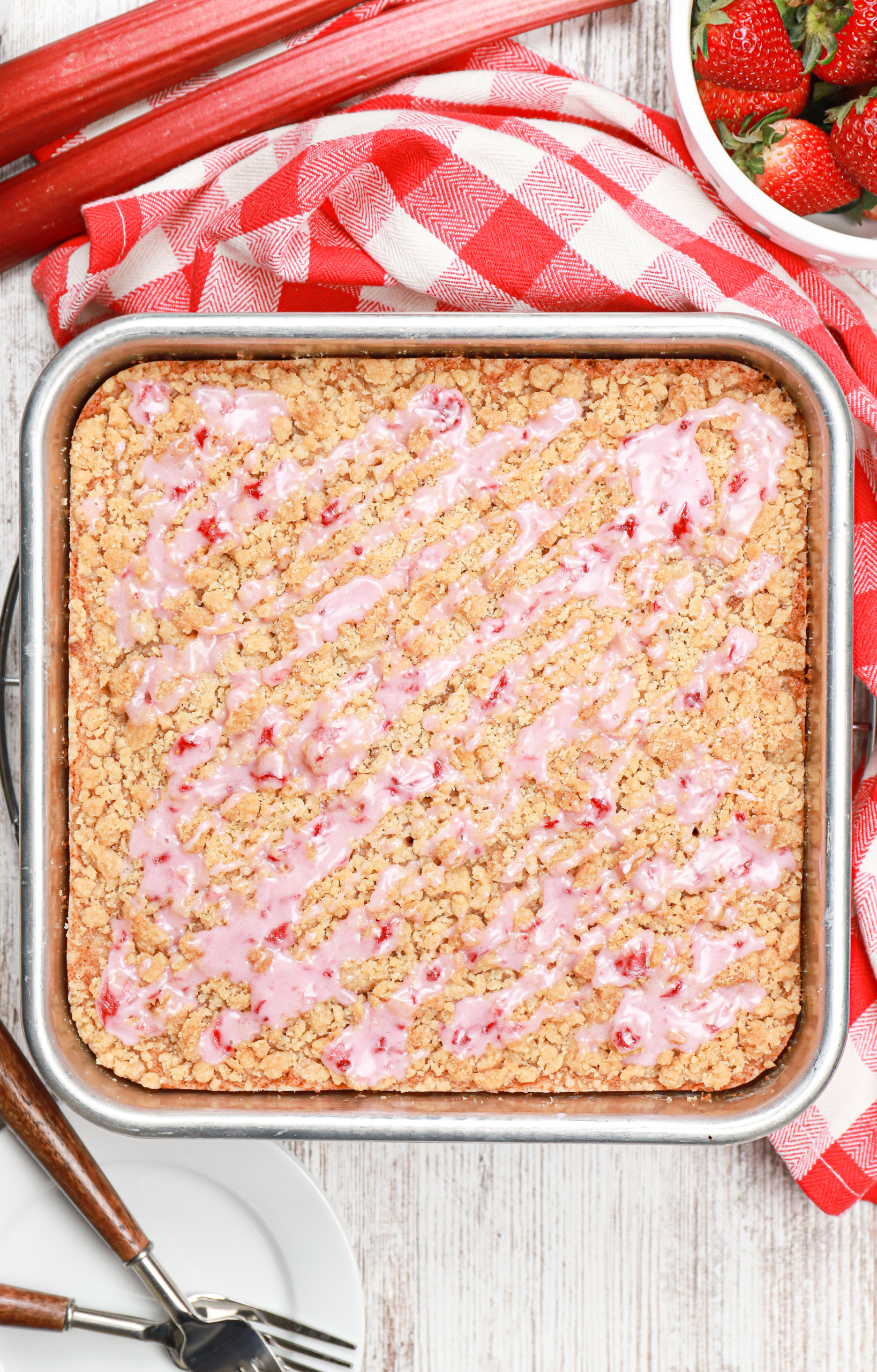 Overhead view of a pan of strawberry rhubarb crumb cake with a strawberry drizzle.