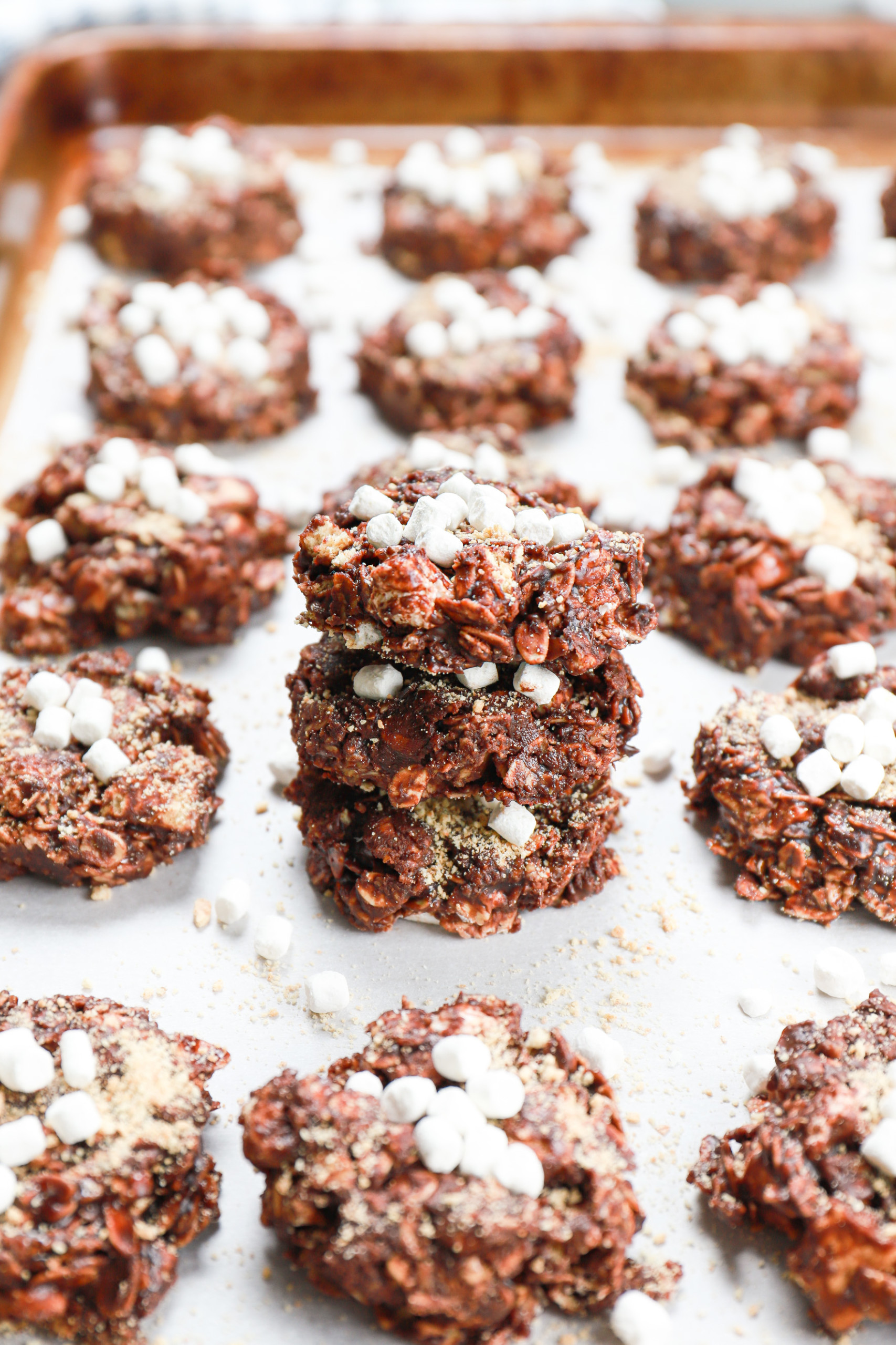 A stack of these dark chocolate smores no bake cookies on a parchment paper covered baking sheet surrounded by more cookies.