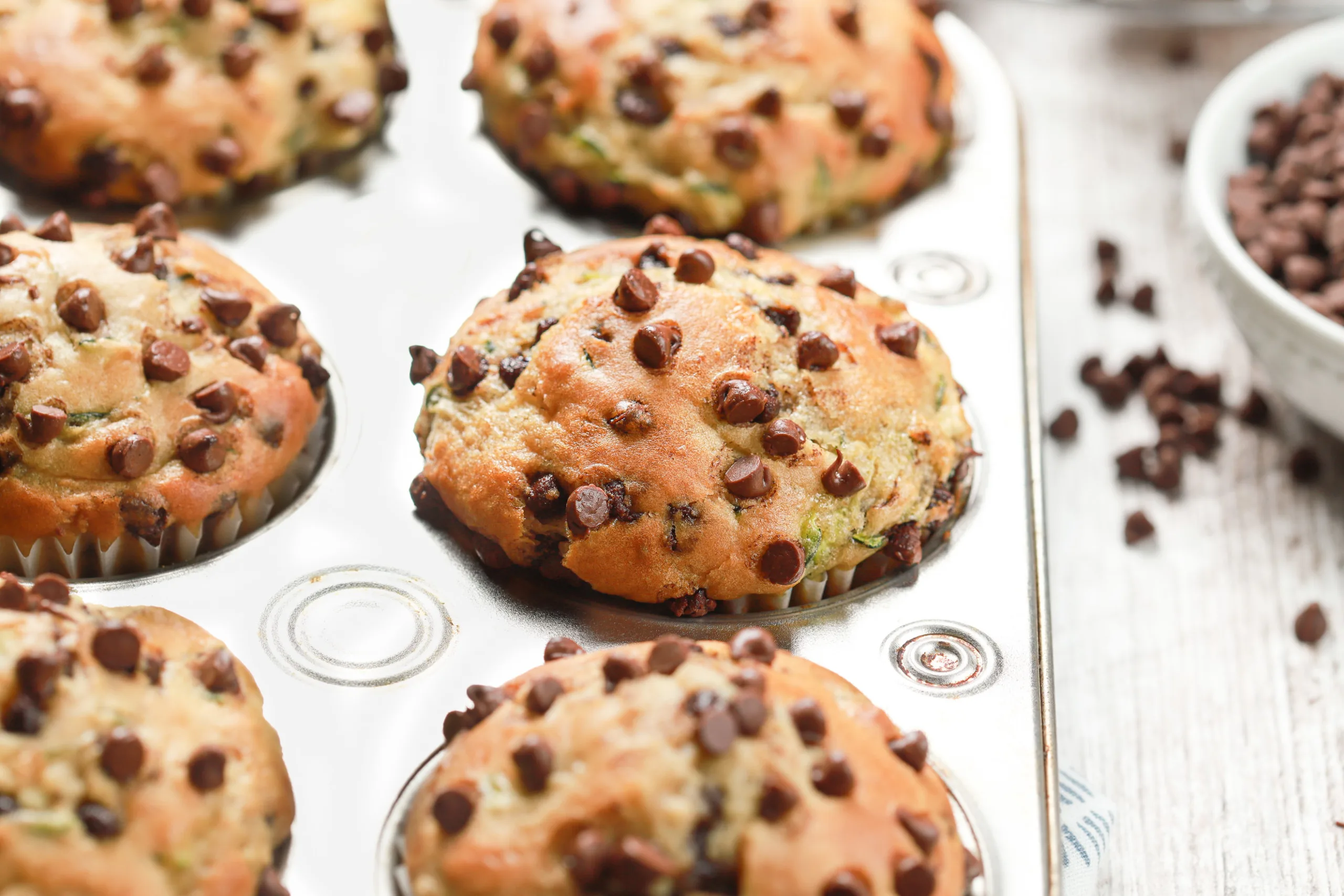 Up close side view of the top of a chocolate chip zucchini muffin in a muffin tin.