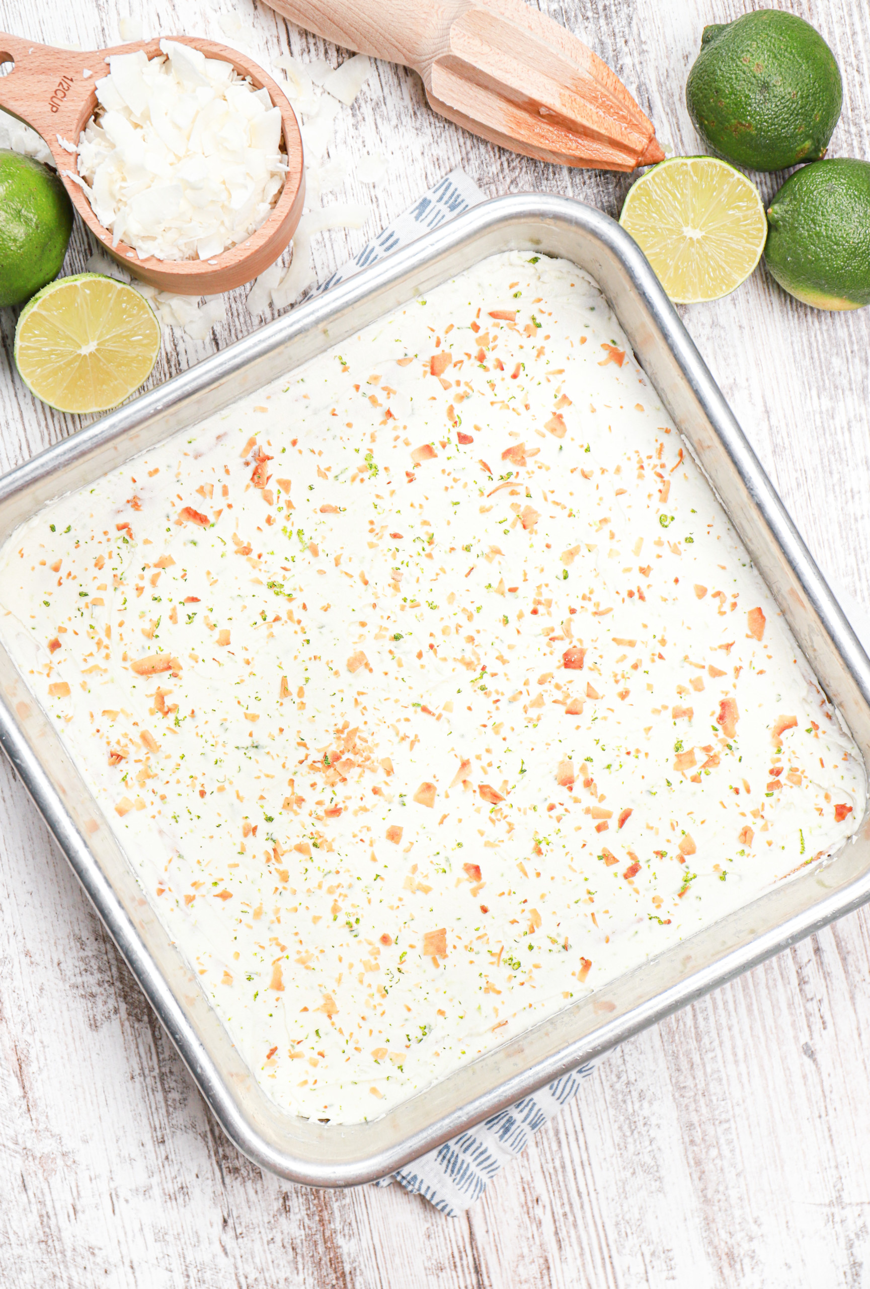 Overhead view of a batch of coconut oat bars in a baking dish frosted with lime frosting.