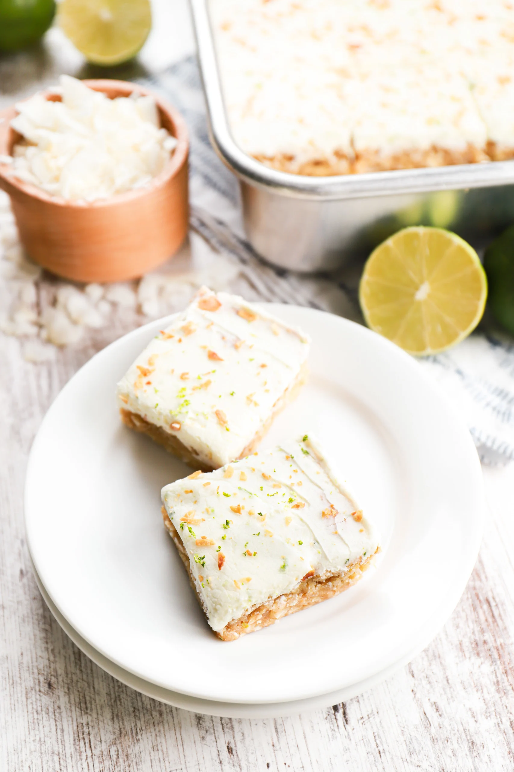 Overhead view of two coconut oat bars on a small white plate with the baking dish full of the remaining bars behind them.