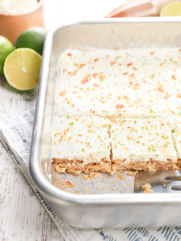 Side view of a row of lime frosted coconut oat bars in a baking dish.