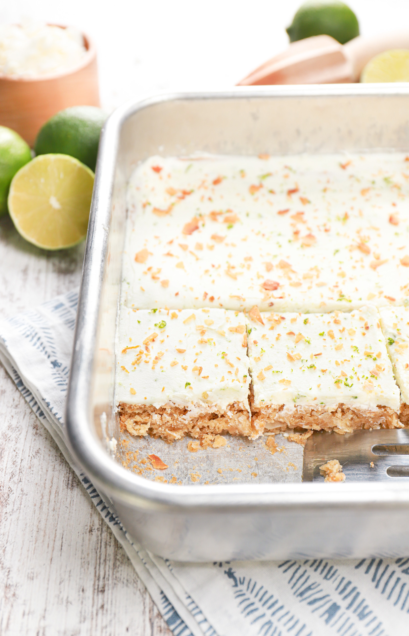 Side view of a row of lime frosted coconut oat bars in a baking dish.