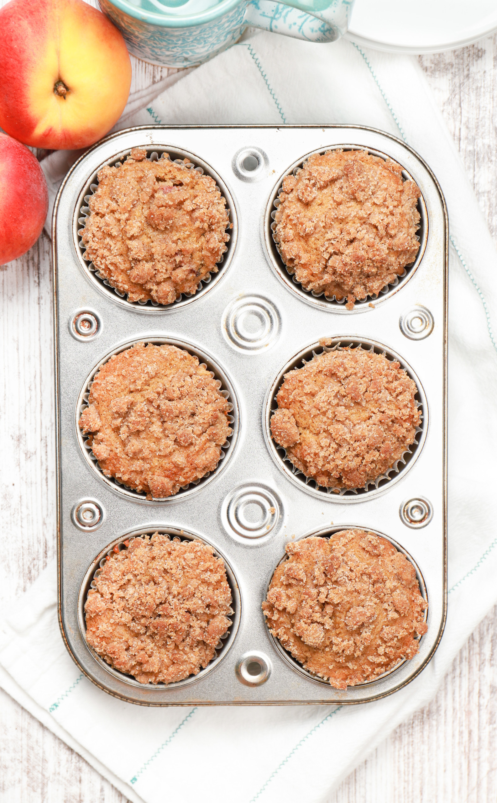 Overhead view of a muffin tin full of peach coffee cake muffins before the drizzle.