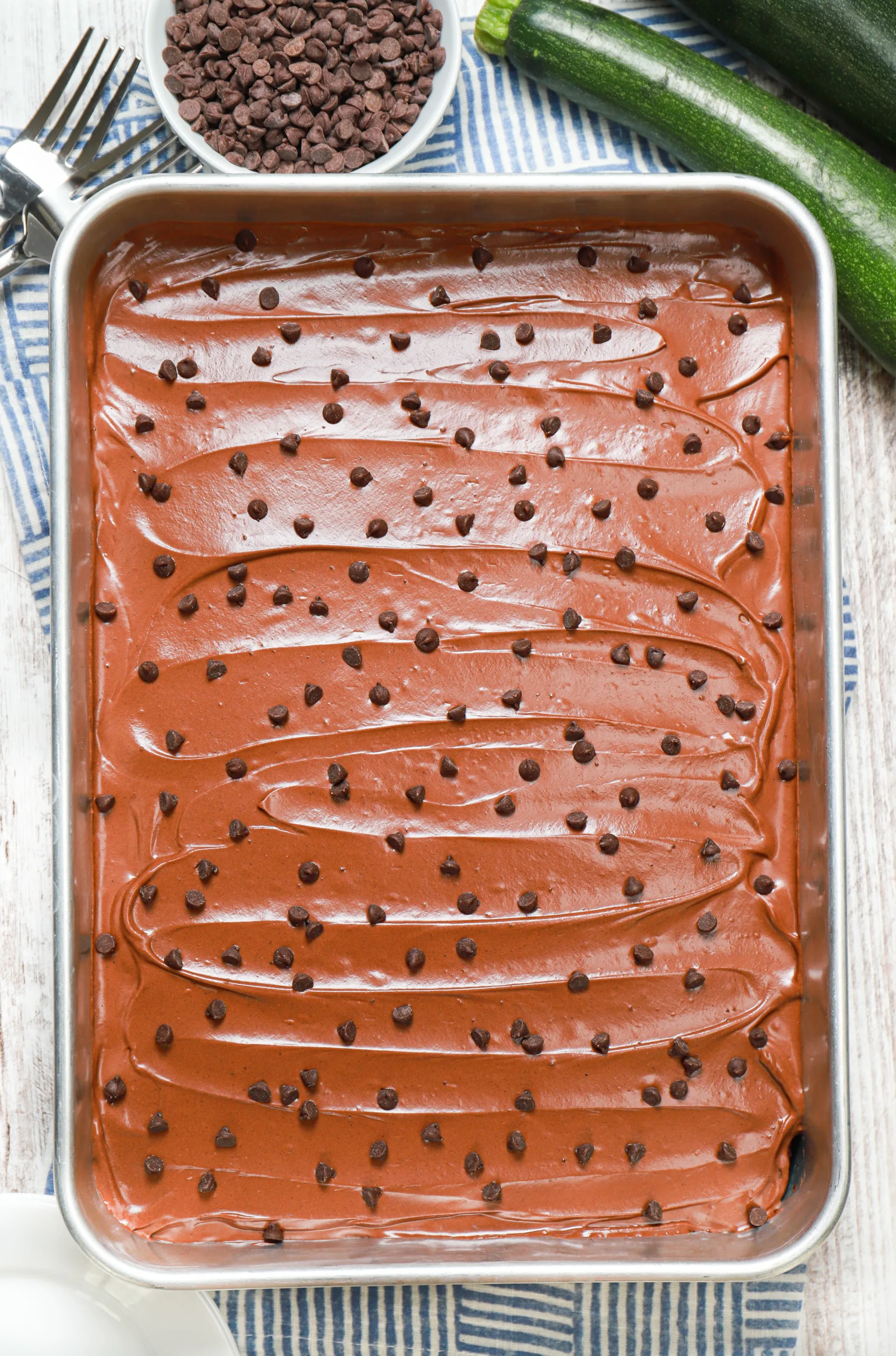 Overhead view of a batch of frosted chocolate zucchini bars in an aluminum baking dish before being cut.