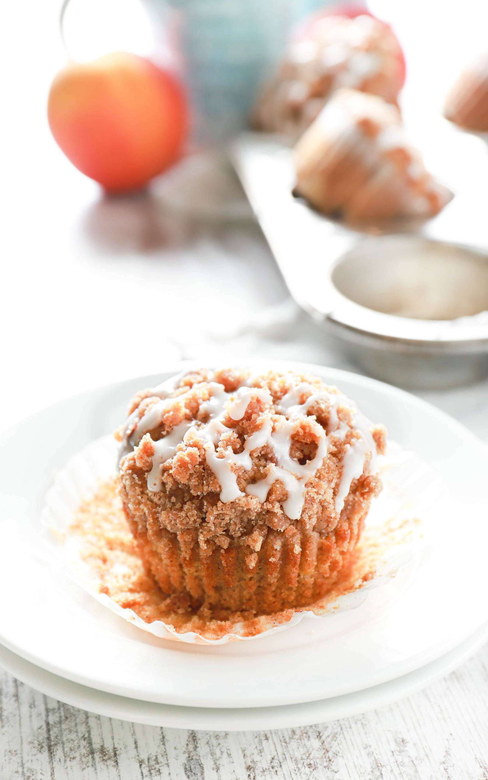A peach coffee cake muffin with the wrapper off on a small white plate.