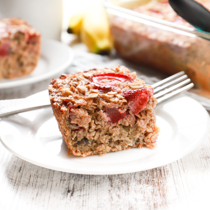 Up close side view of a piece of strawberry banana bread baked oatmeal on a small white plate.