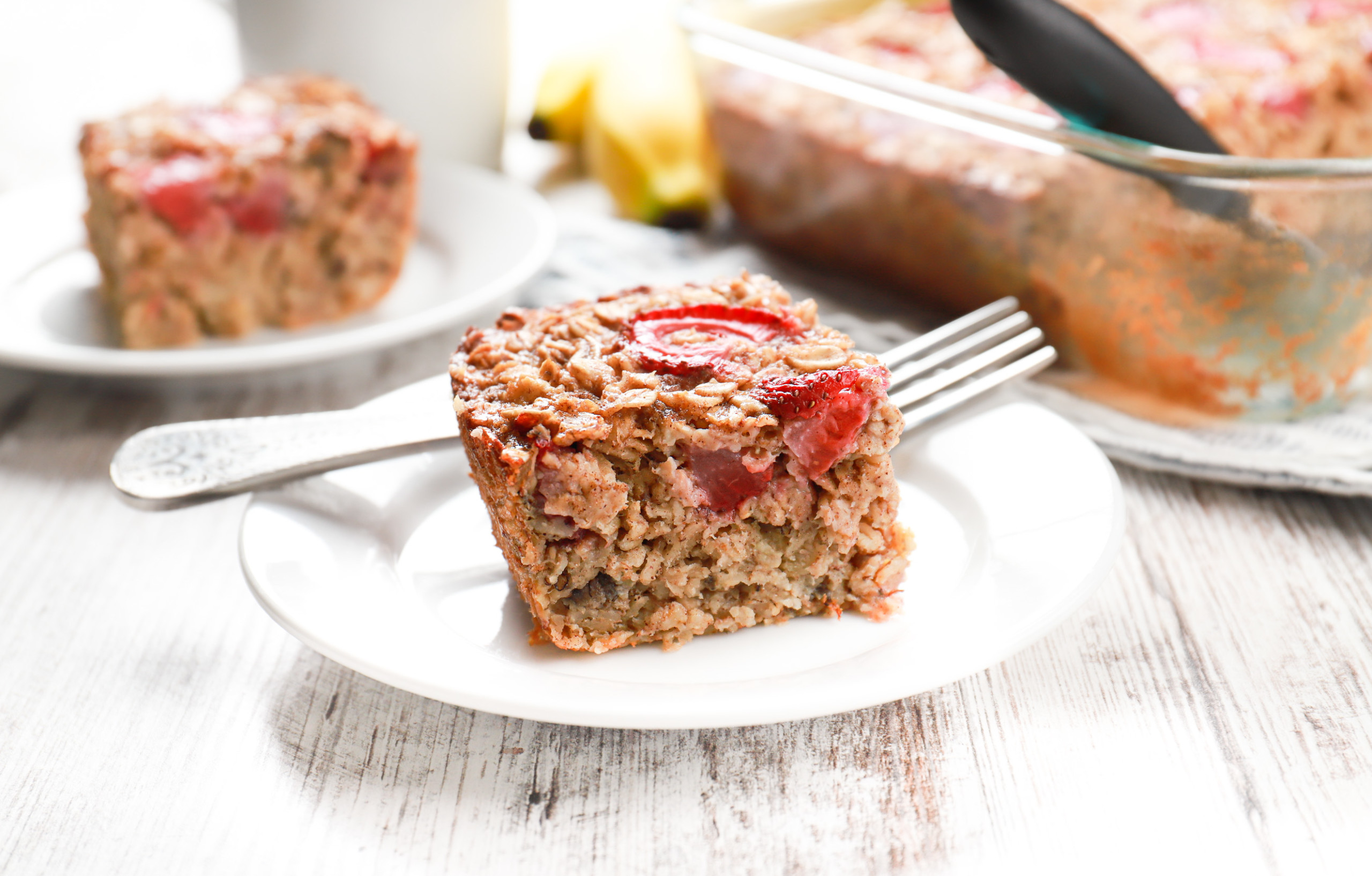 Up close side view of a piece of strawberry banana bread baked oatmeal on a small white plate.