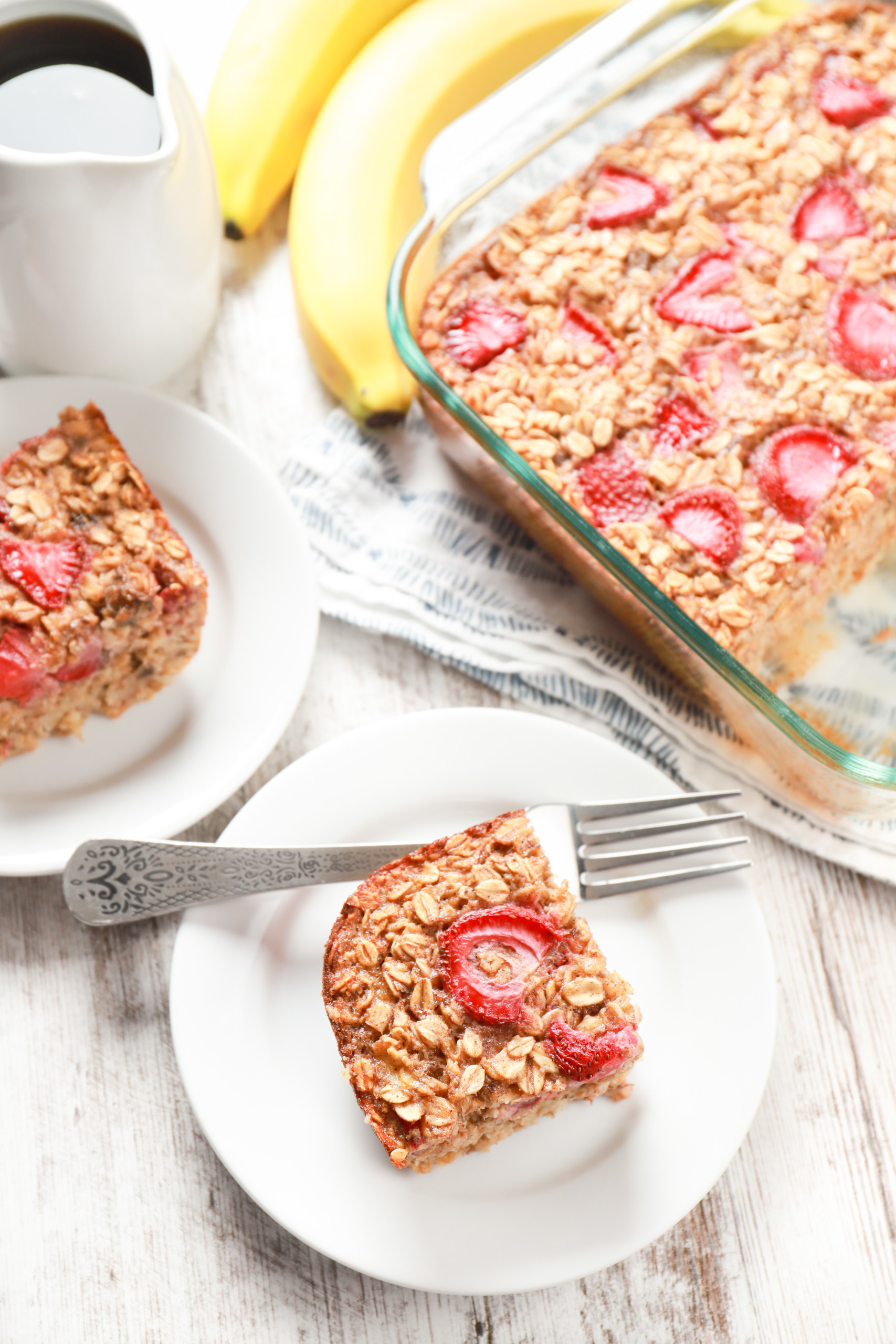 Overhead view of two pieces of strawberry banana bread baked oatmeal on small white plate with the remaining oatmeal in the background.