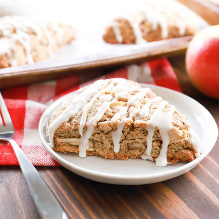 Side view of a cinnamon apple scone on a small white plate with the remainder of the scones on the baking sheet in the background.