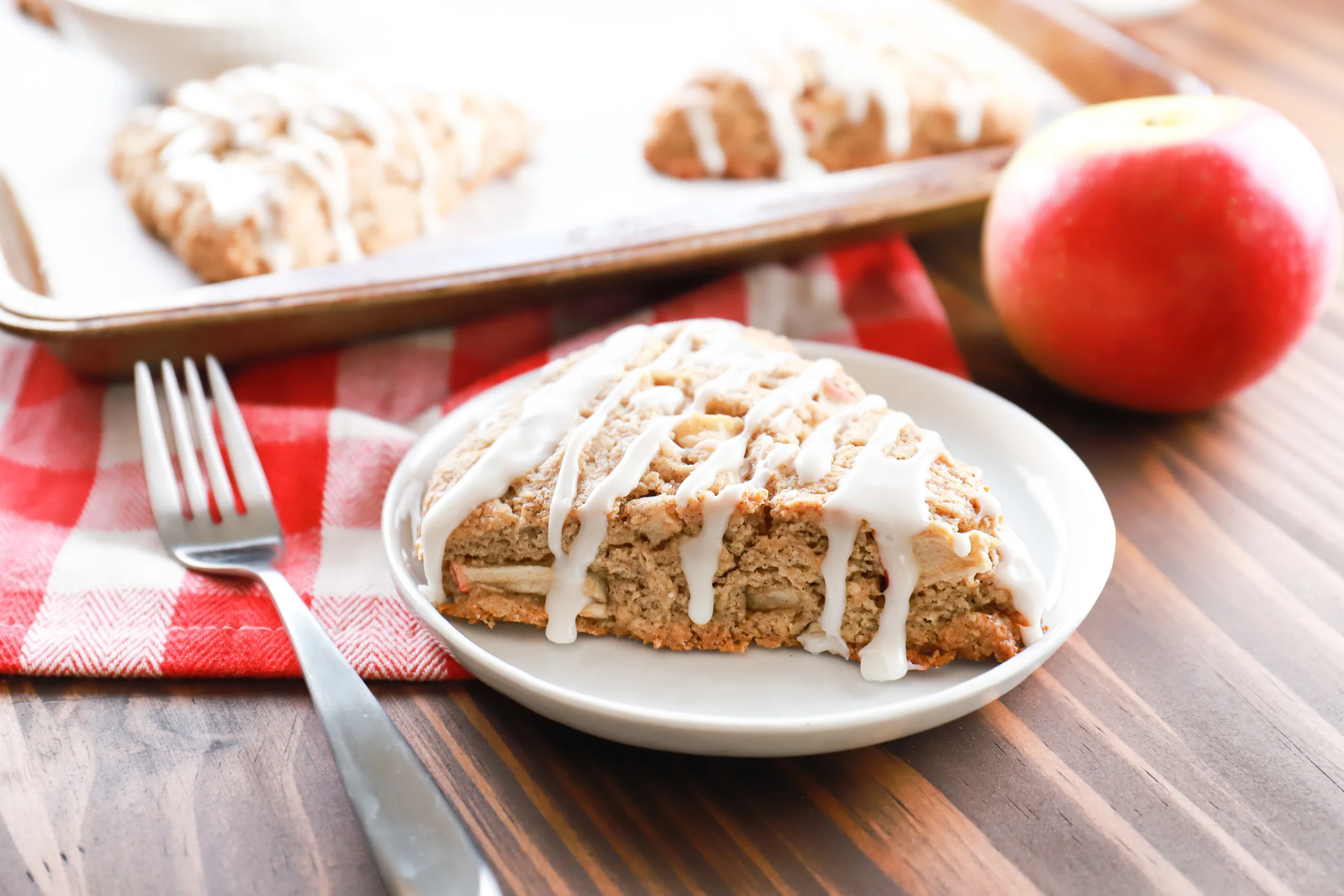 Side view of a cinnamon apple scone on a small white plate with the remainder of the scones on the baking sheet in the background.