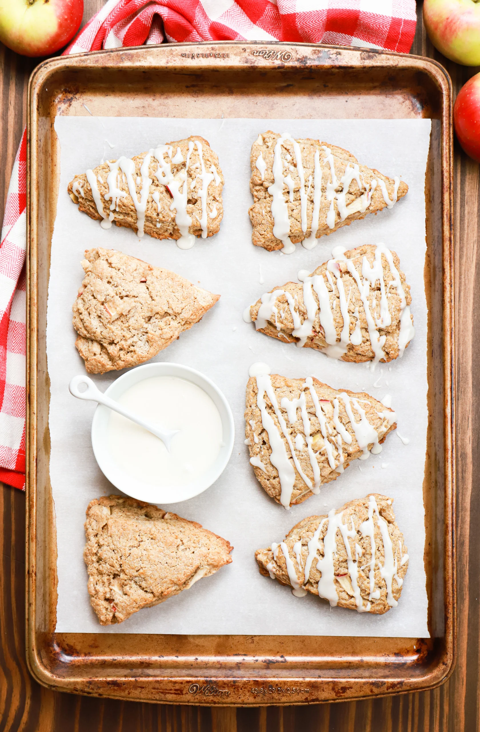 Overhead view of a batch of apple cinnamon scones with some of them drizzled with a vanilla glaze.