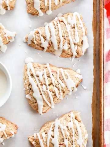 Up close overhead view of a few apple cinnamon scones on a parchment paper lined baking sheet.