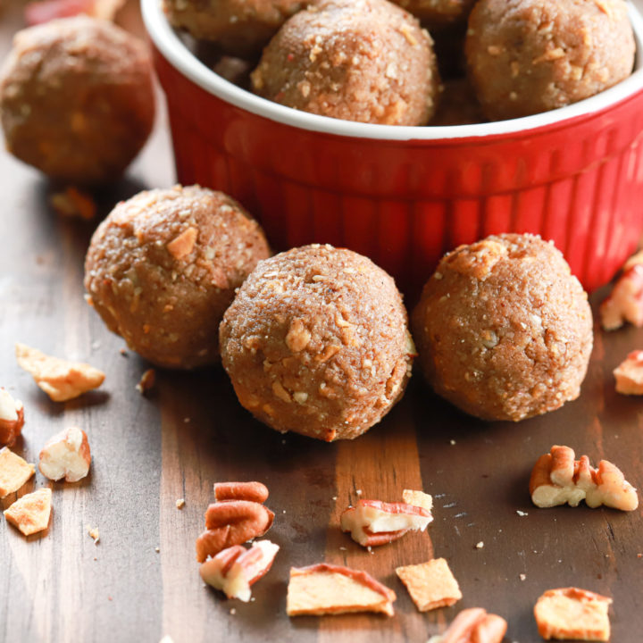 Up close side view of three apple pie protein bites in front of a small red bowl full of protein bites.