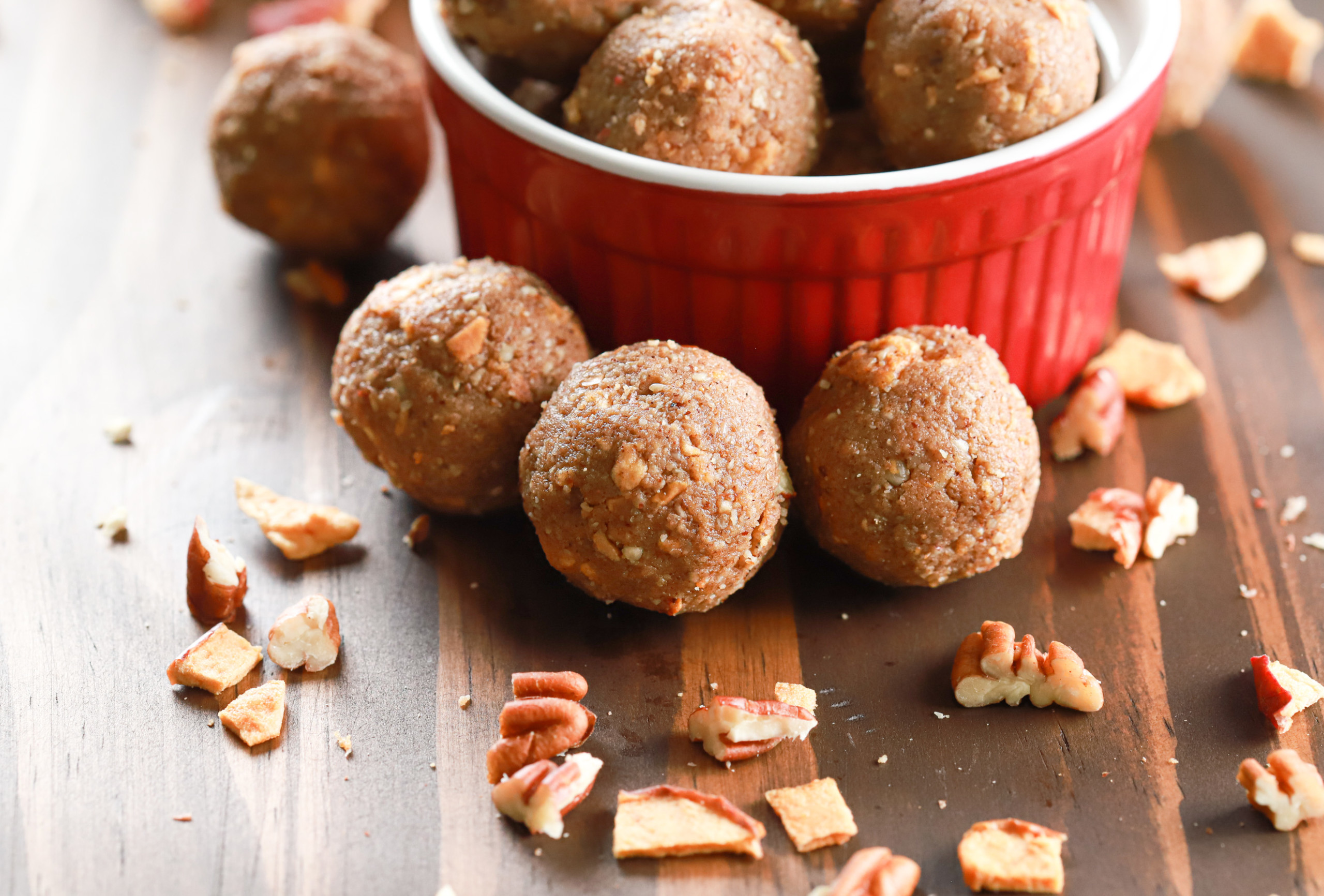 Up close side view of three apple pie protein bites in front of a small red bowl full of protein bites.