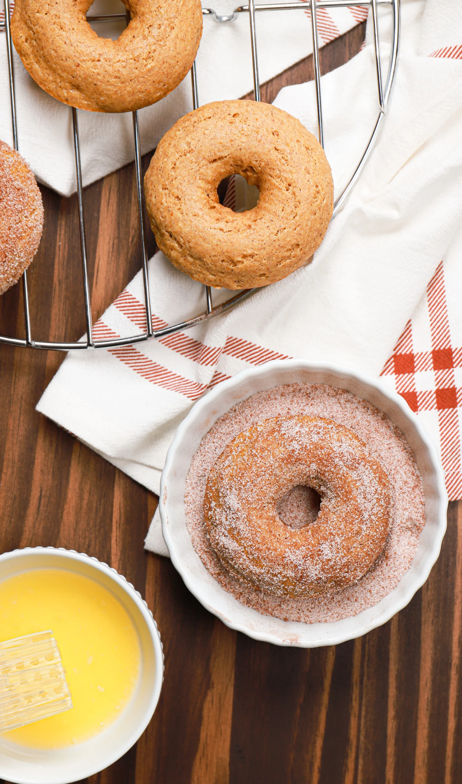 Overhead view of a cinnamon sugar pumpkin donut getting a sugar coating after being brushed with butter.