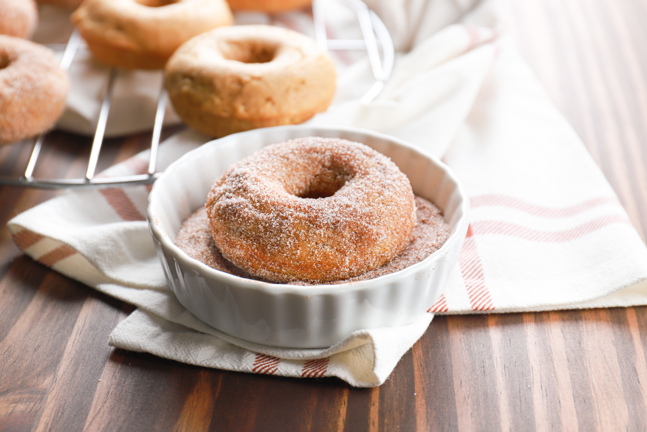 Side view of a cinnamon sugar pumpkin donut in a white bowl filled with cinnamon sugar.