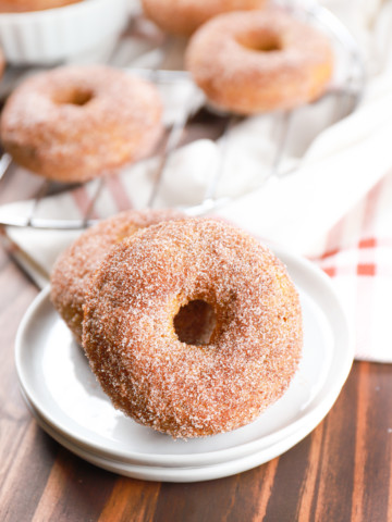 Side view of two cinnamon sugar pumpkin donuts on a small white plate.