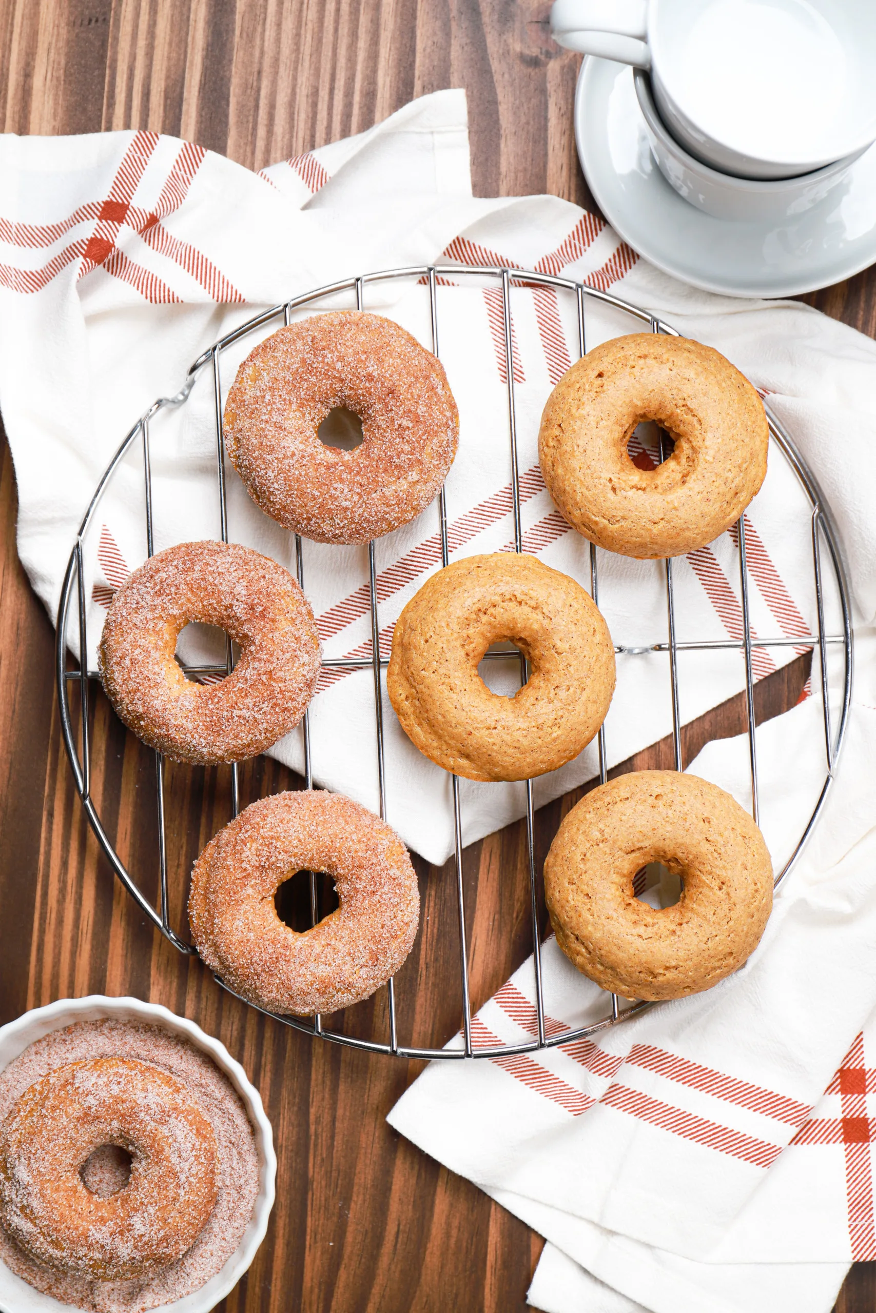 Overhead view of cinnamon sugar pumpkin donuts on a wire rack with half of the donuts having the sugar coating and half of the donuts without the sugar coating.