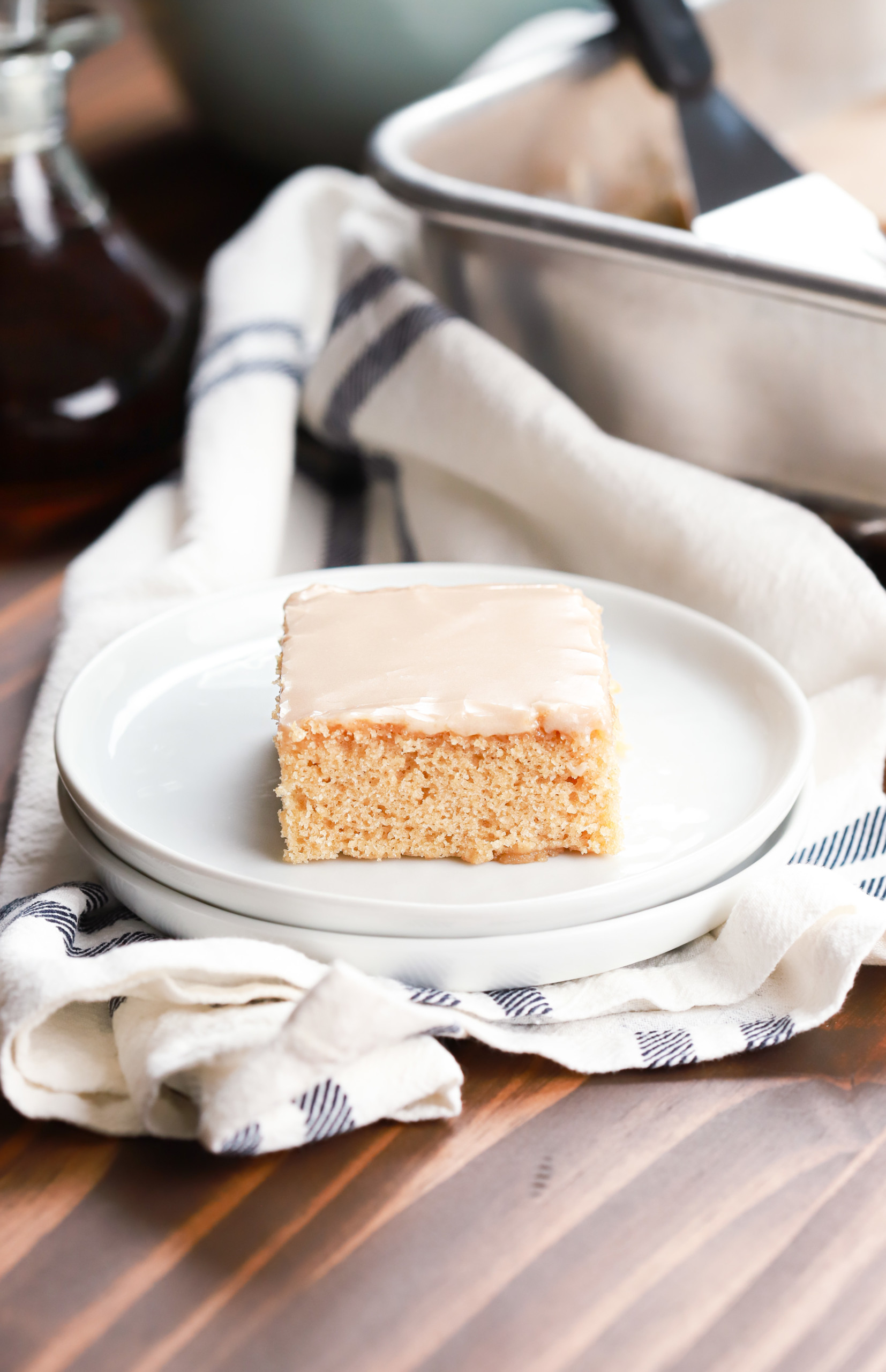 Side view of a maple blondie bar on a small white plate with the remaining bars in the background.