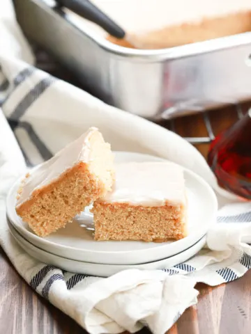 Side view of two maple blondies on a small white plate with the baking dish of remaining bars in the background.