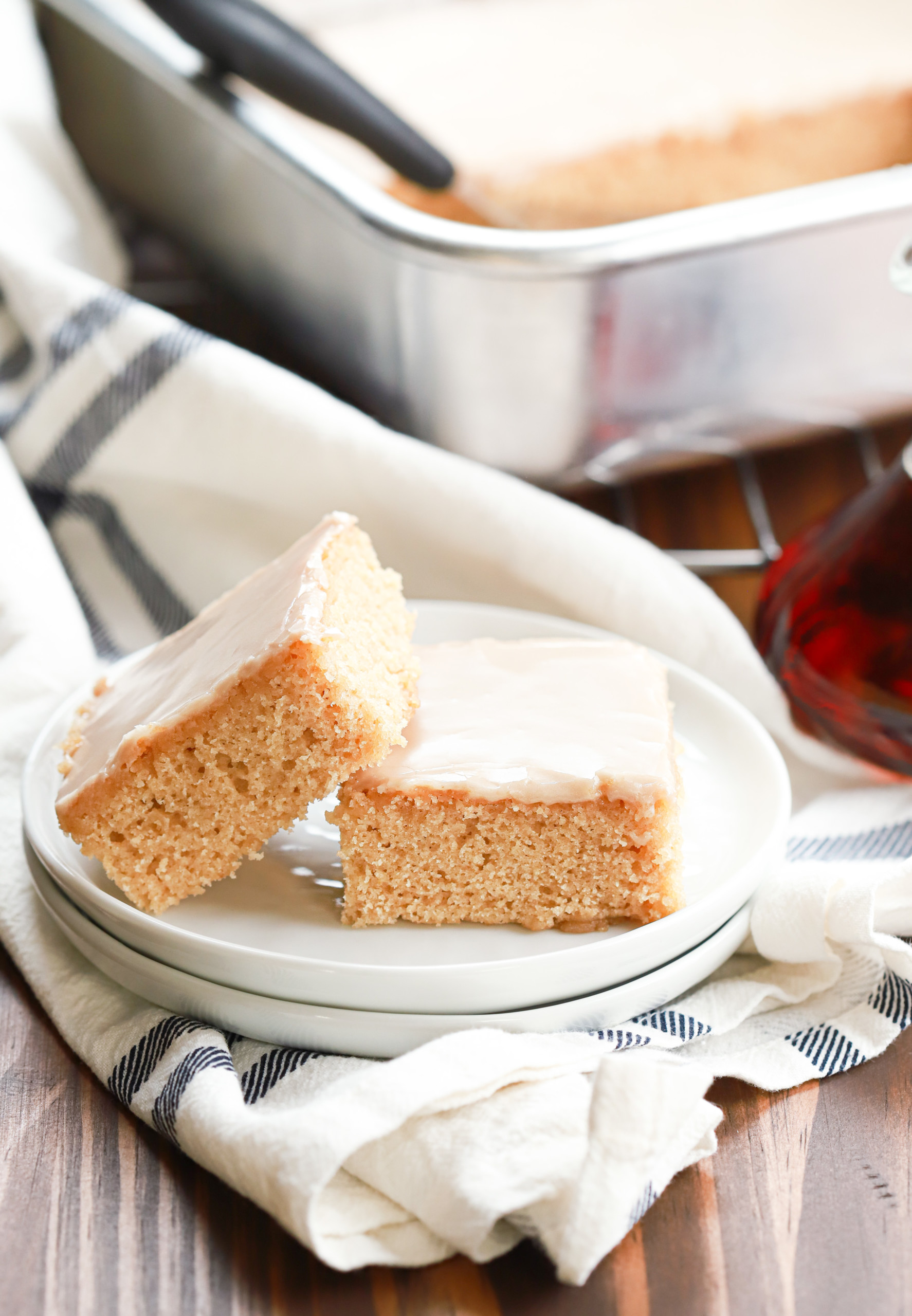 Side view of two maple blondies on a small white plate with the baking dish of remaining bars in the background.