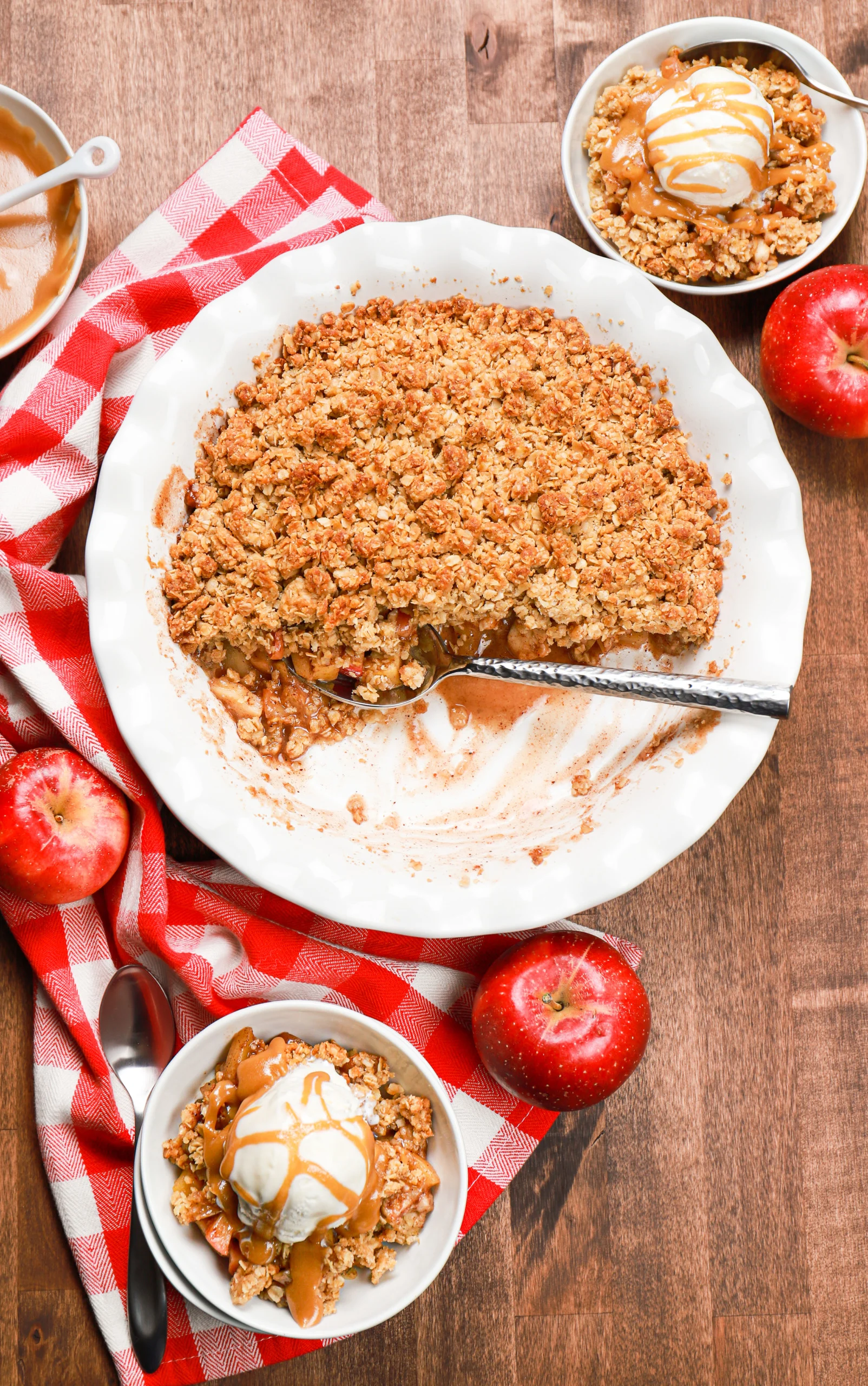 Overhead view of the pie plate of apple crisp half gone and two small white bowls on the top and bottom of the pie plate filled with caramel apple crisp.