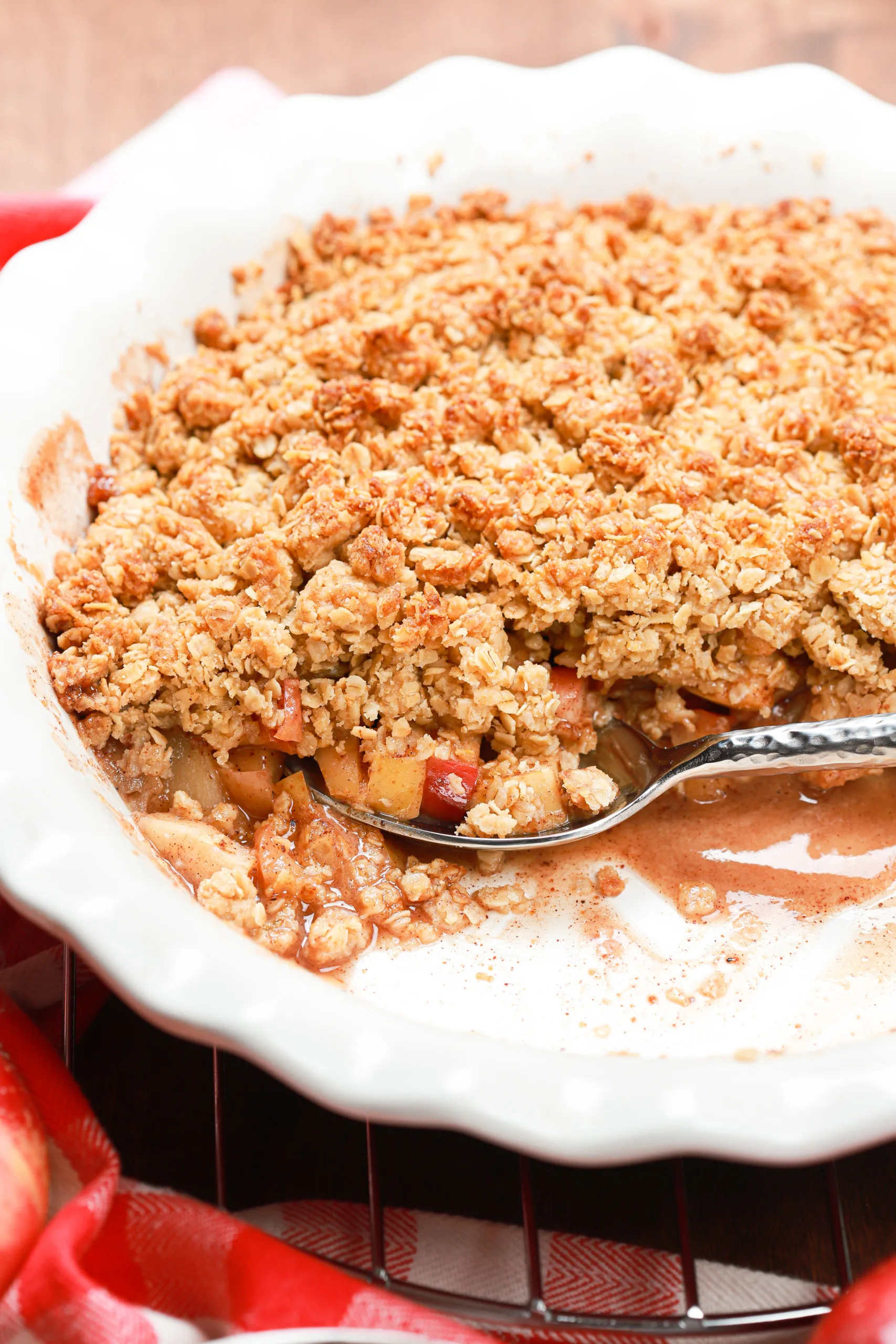 Side view of a scoop of caramel apple crisp in a pie plate surrounded by a red checked cloth.