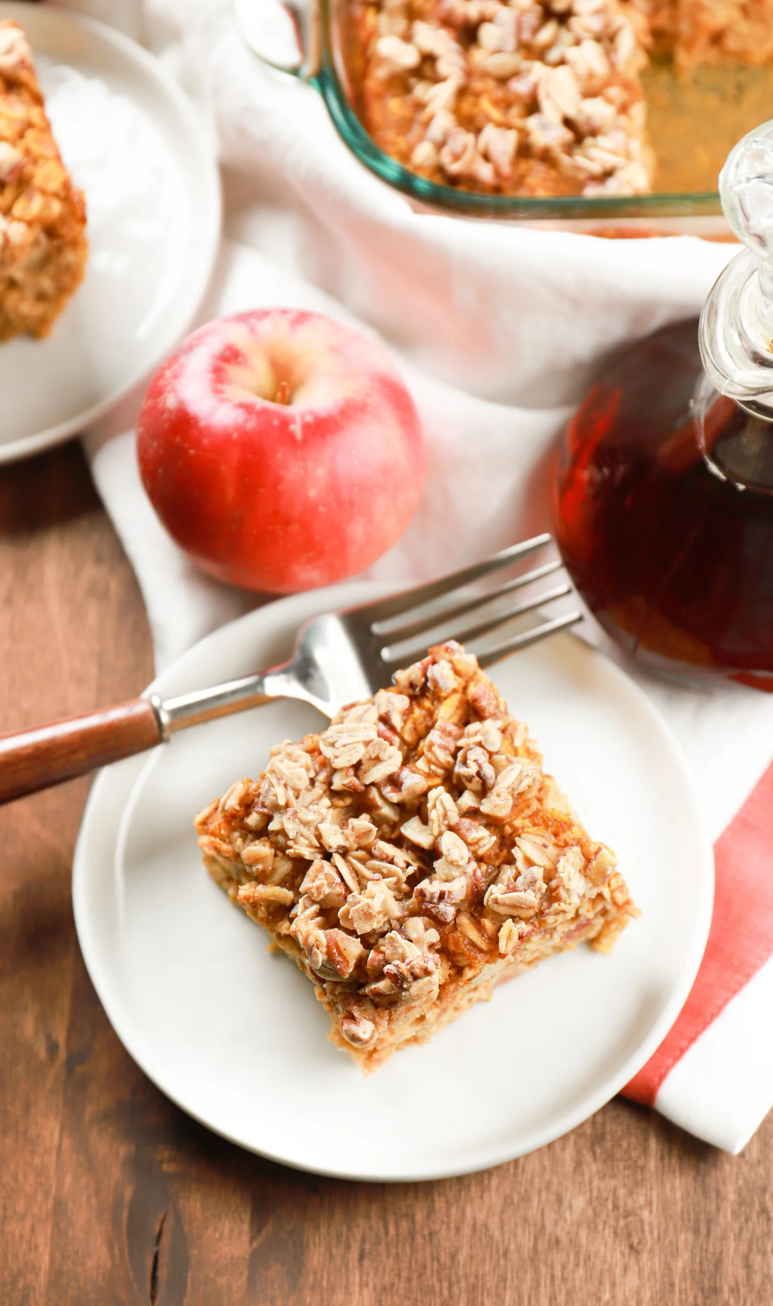 Overhead view of a piece of apple pumpkin baked oatmeal on a small white plate with another piece and the remaining batch behind it.