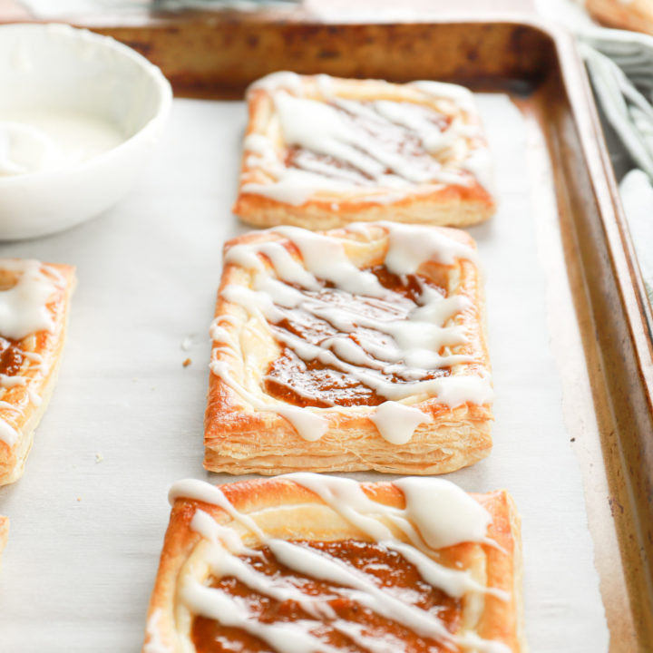 Up close side view to show the flaky layers of a pumpkin cream cheese danish on a baking sheet.