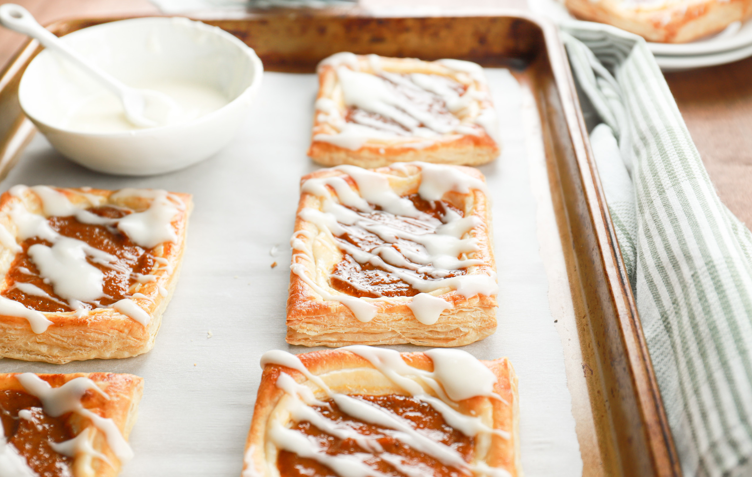 Up close side view to show the flaky layers of a pumpkin cream cheese danish on a baking sheet.