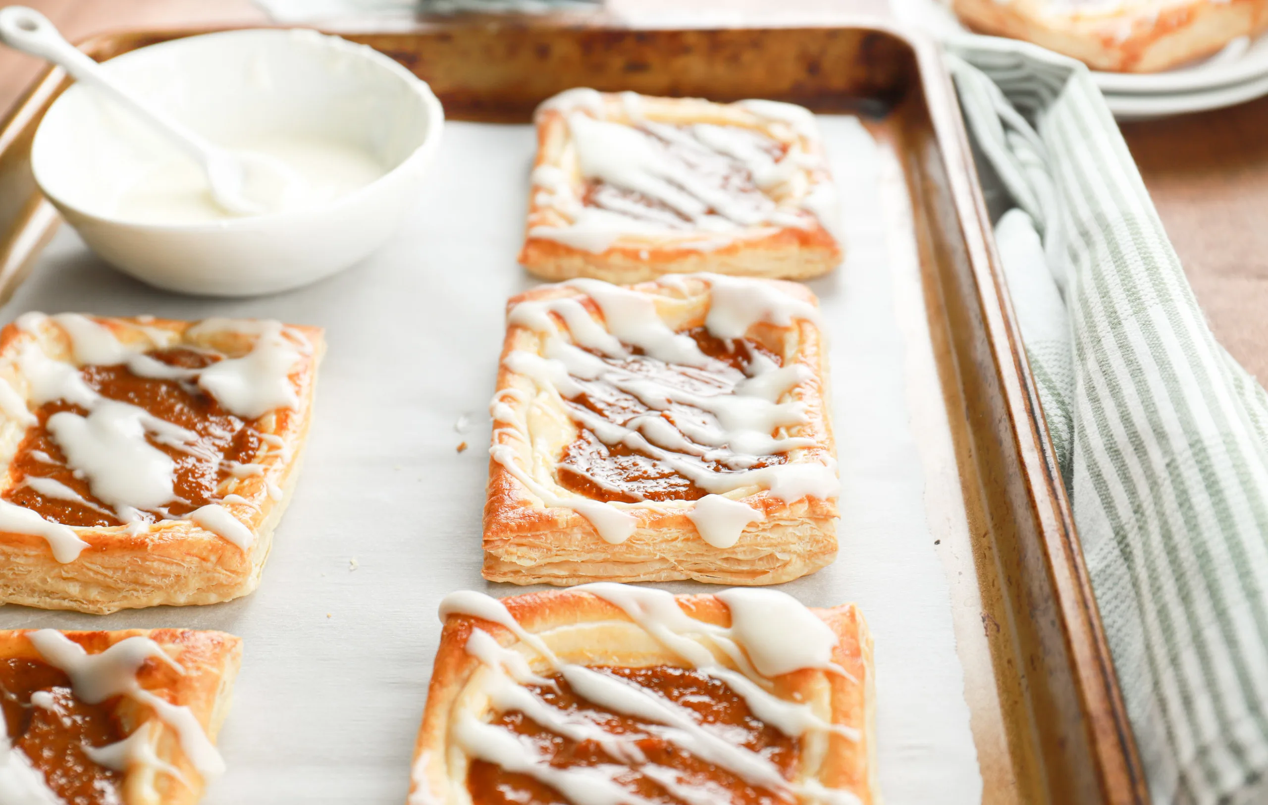 Up close side view to show the flaky layers of a pumpkin cream cheese danish on a baking sheet.